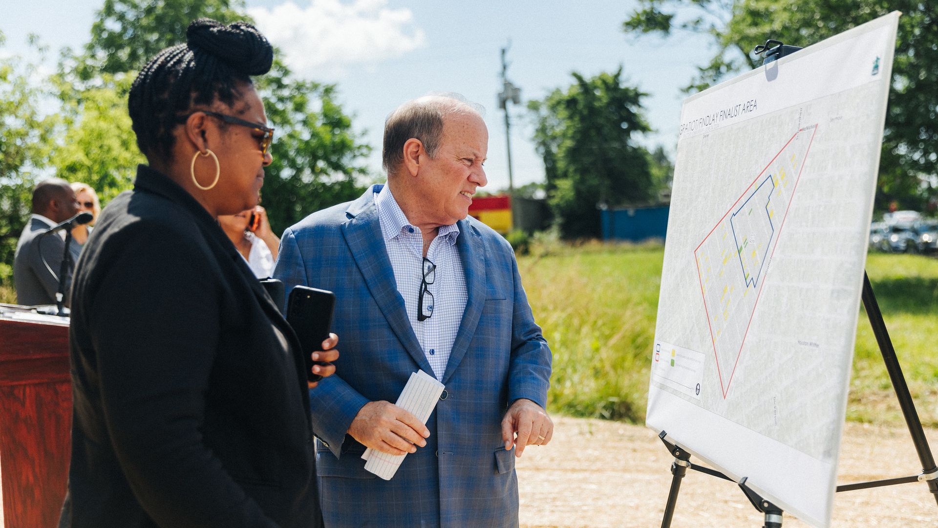Mayor Mike Duggan looks at a sign showing a map of a solar neighborhood during a press conference outdoors. 