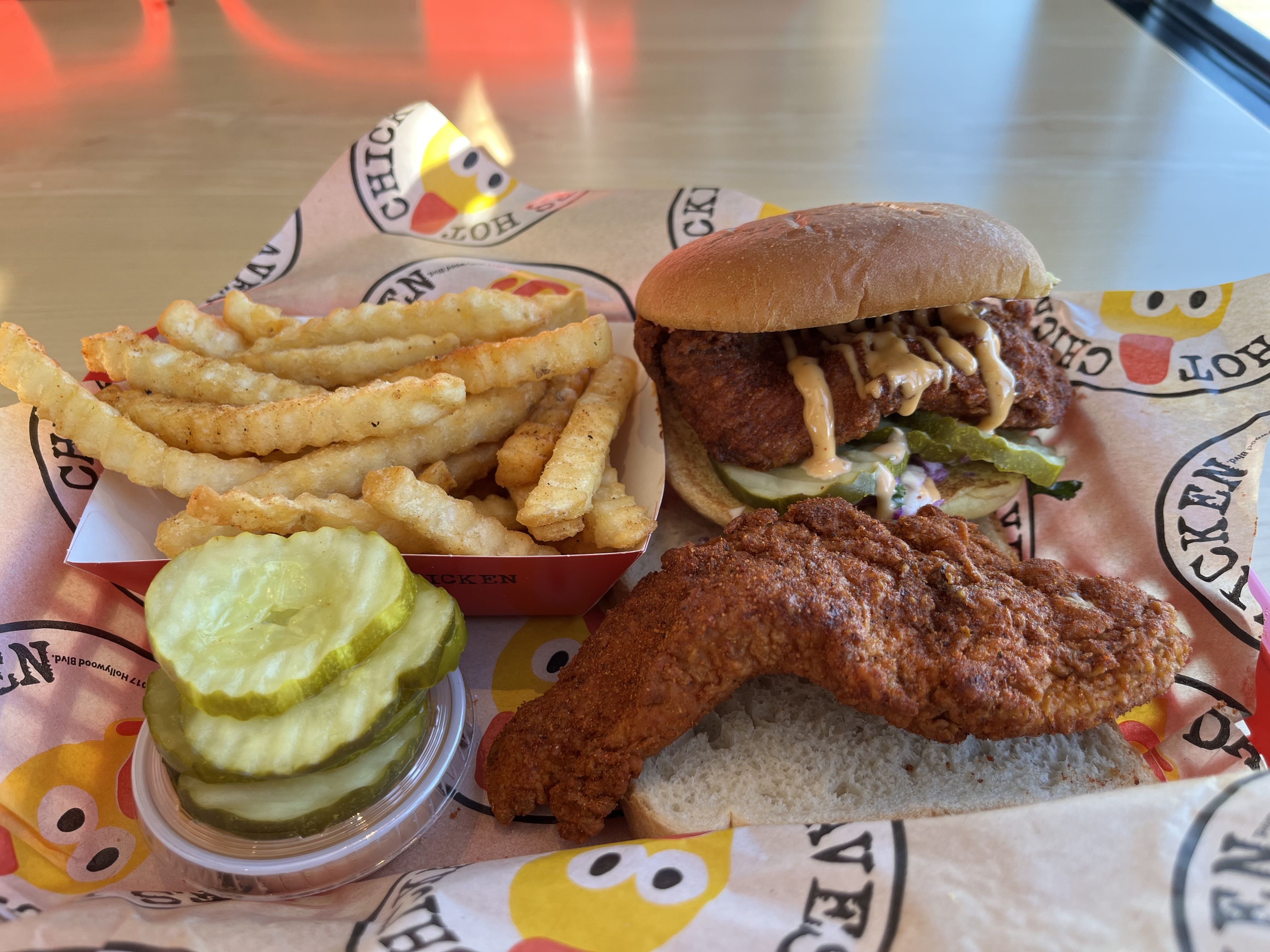 A chicken sandwich, tender and fries with pickles and slaw atop the sandwhich 