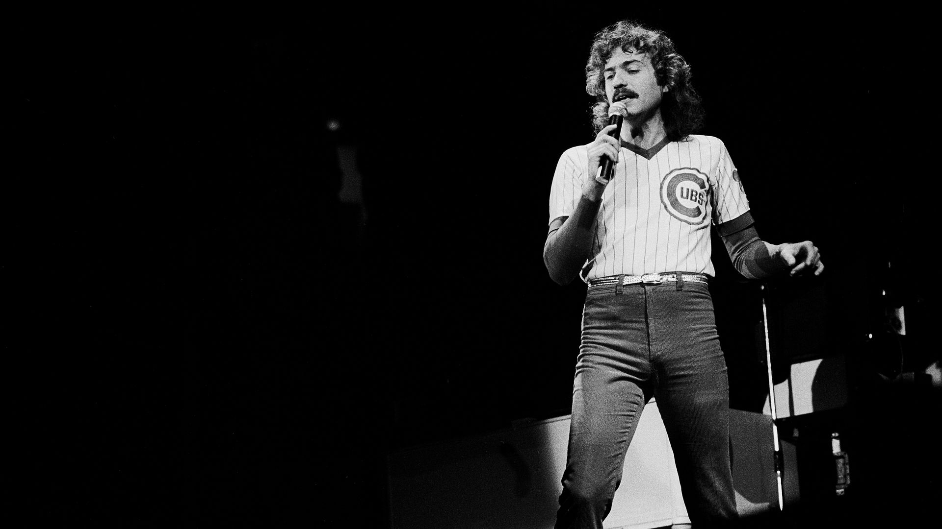 Photo of a man in a Cubs shirt holding a microphone on stage 