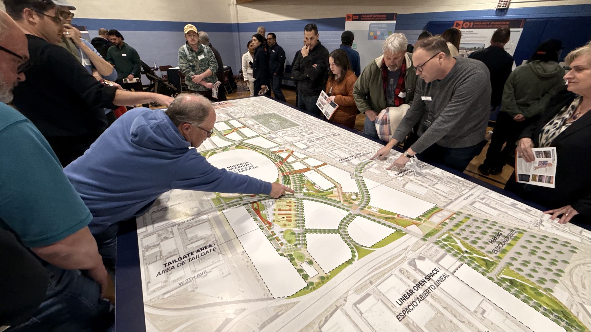 Group of people gathered around a large table reviewing a detailed urban planning map with labels and schematics. 