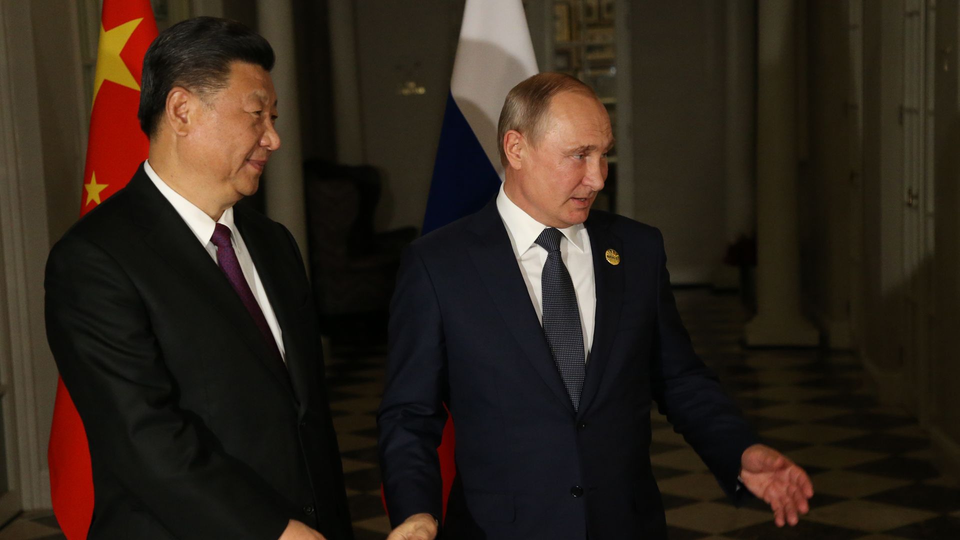 Chinese president Xi Jinping stands next to Russian president Vladimir Putin in front of both countries' flags
