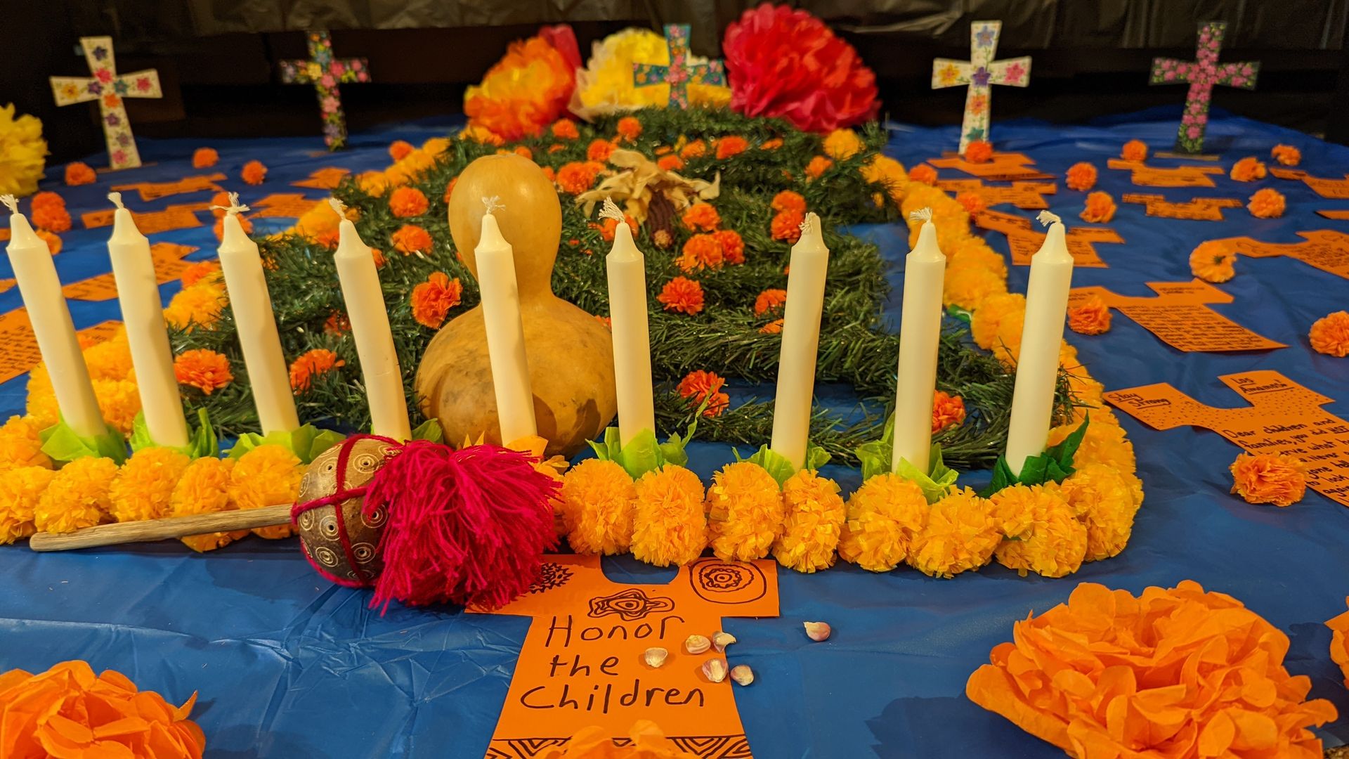 A paper shaped like a t-shirt says "Honor the children" in front of candles and a paper grave covered with paper flowers, with crosses in the background.