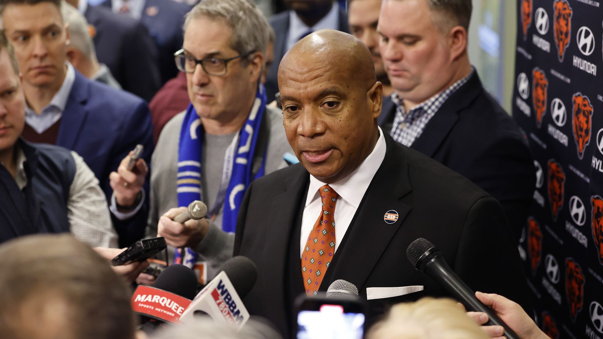 Photo of a man in a suit talking to other men who are holding microphones