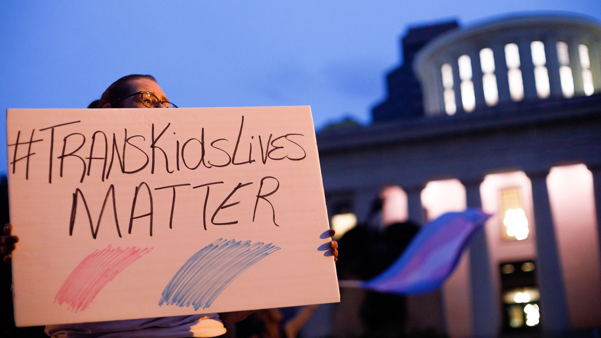 Photo of a person holding a sign that says "#TransKidsLives matter"
