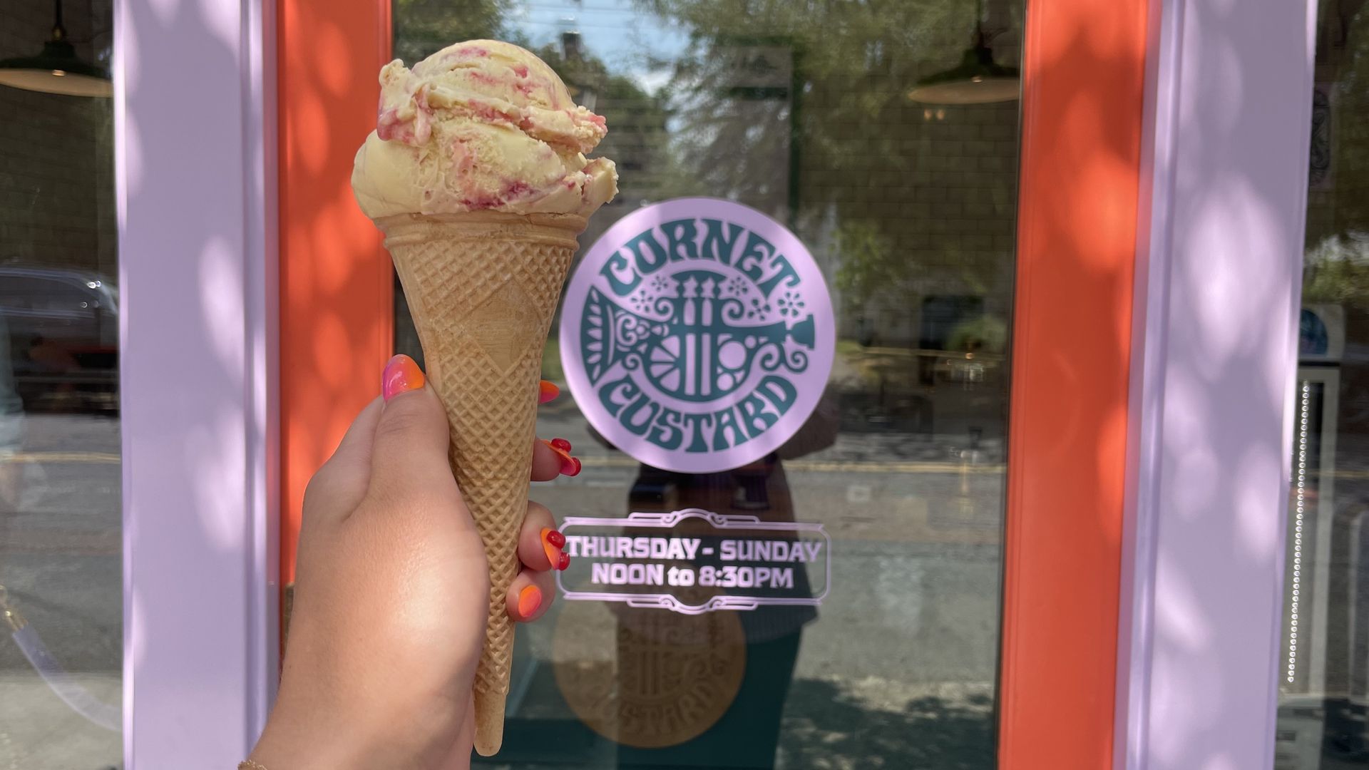 A photo of a hand holding an ice cream cone next to a doorway with a sign that reads "Cornet Custard"