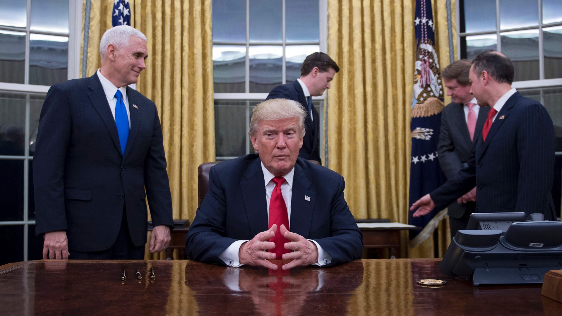 Donald Trump sits at his desk as his staff works around him