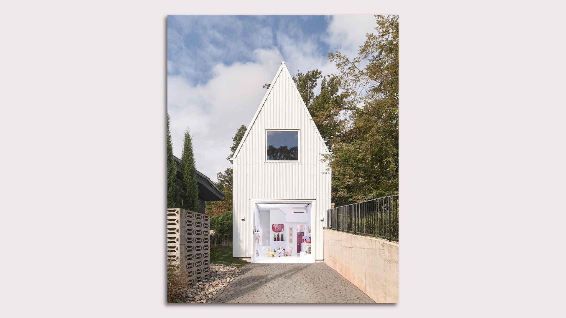 A photo showing the exterior of a garage turned into an art gallery, with white siding and a pointed roof.