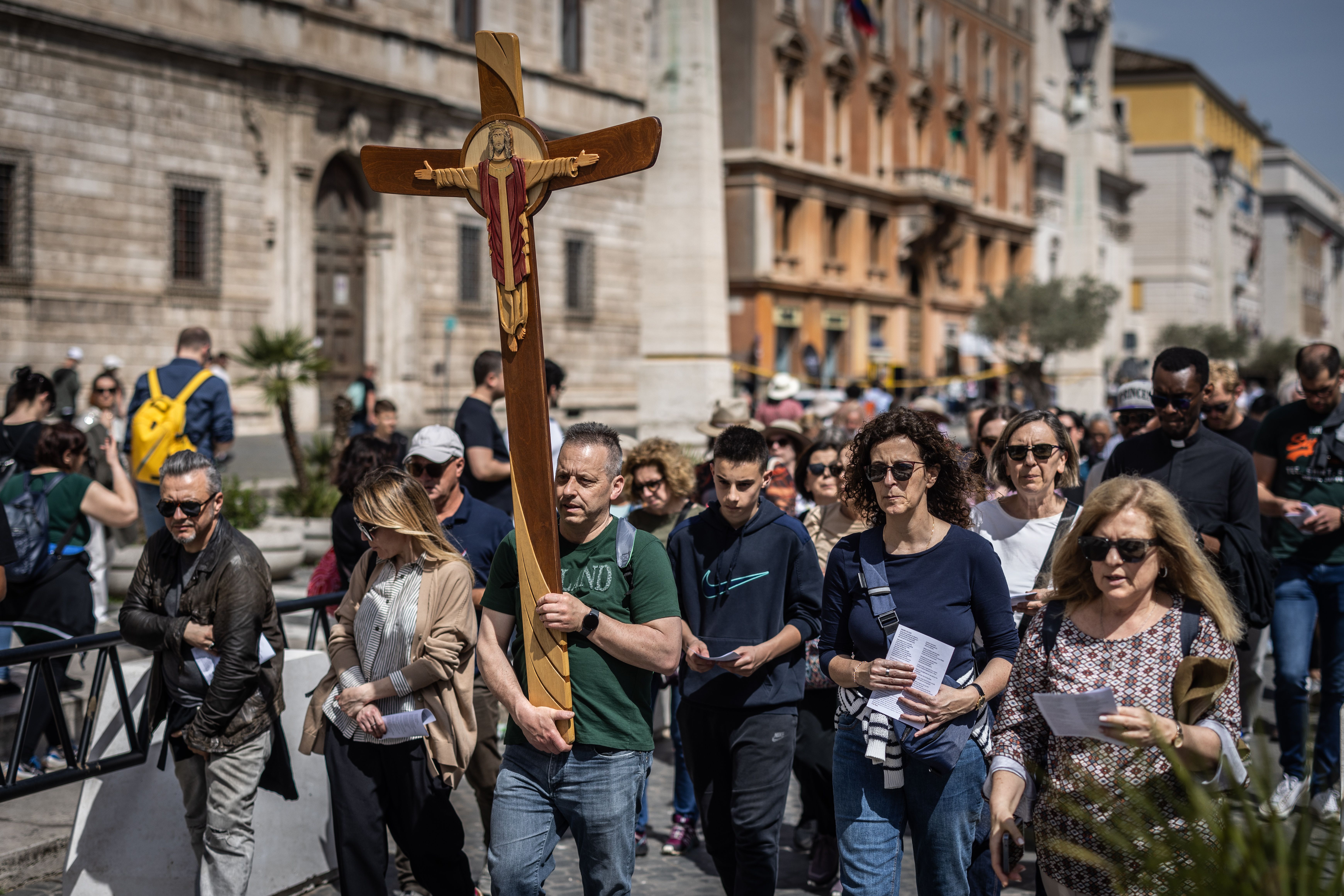 People walk through street holding a cross 
