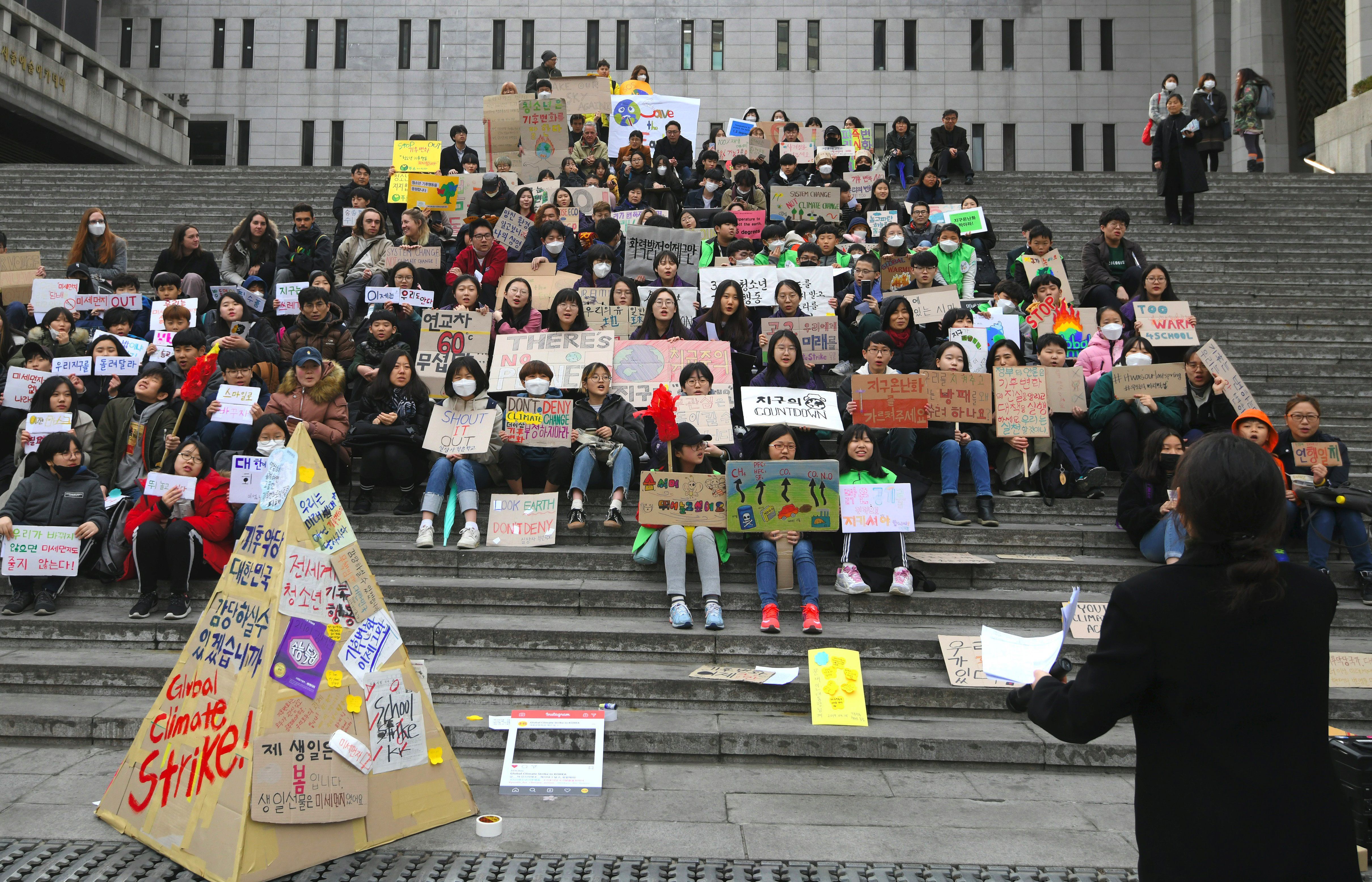 South Korean protestors sit on steps with their signs, next to a teepee made out of more signs.