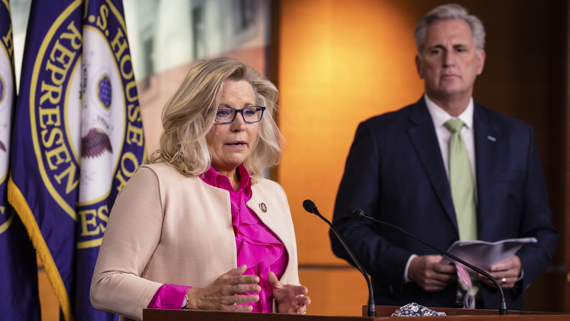 Photo of Liz Cheney speaking from a podium as Kevin McCarthy watches from behind her