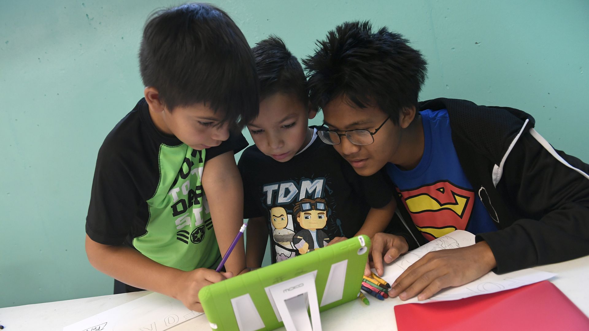Three boys crowd around a tablet on a table