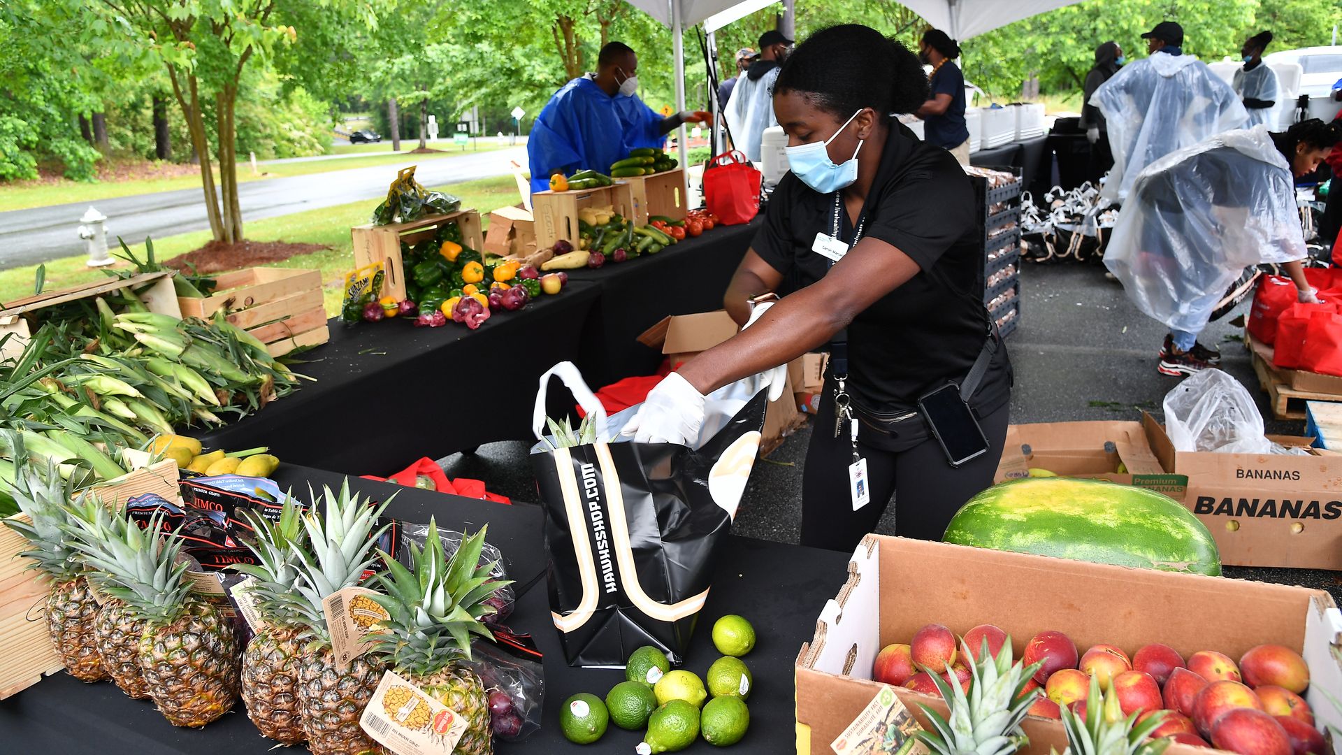 In this image, a woman wearing a face mask puts fruit into a bag 