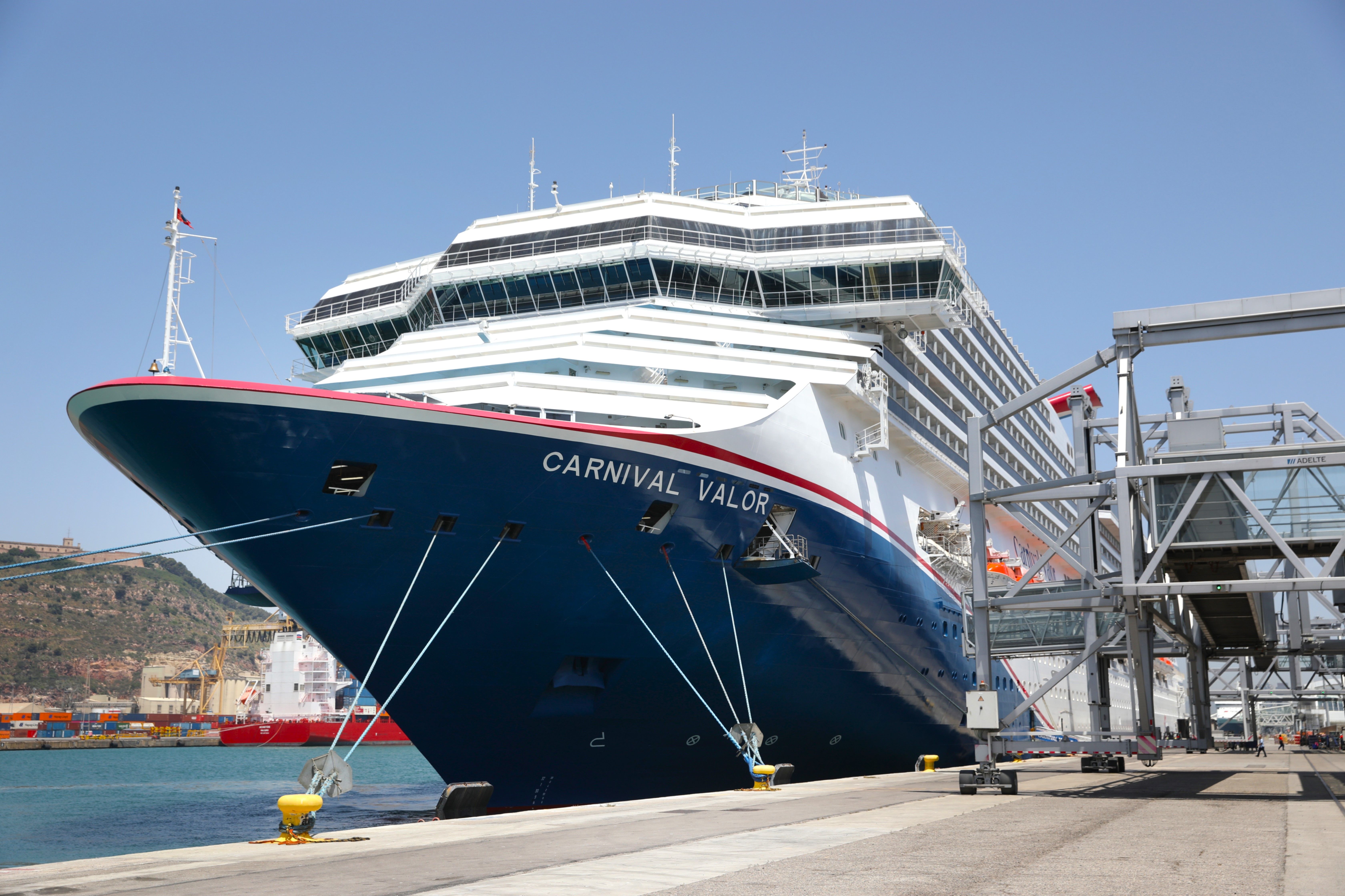 Image shows the red, white and blue hull of Carnival Valor while it is docked in Barcelona.