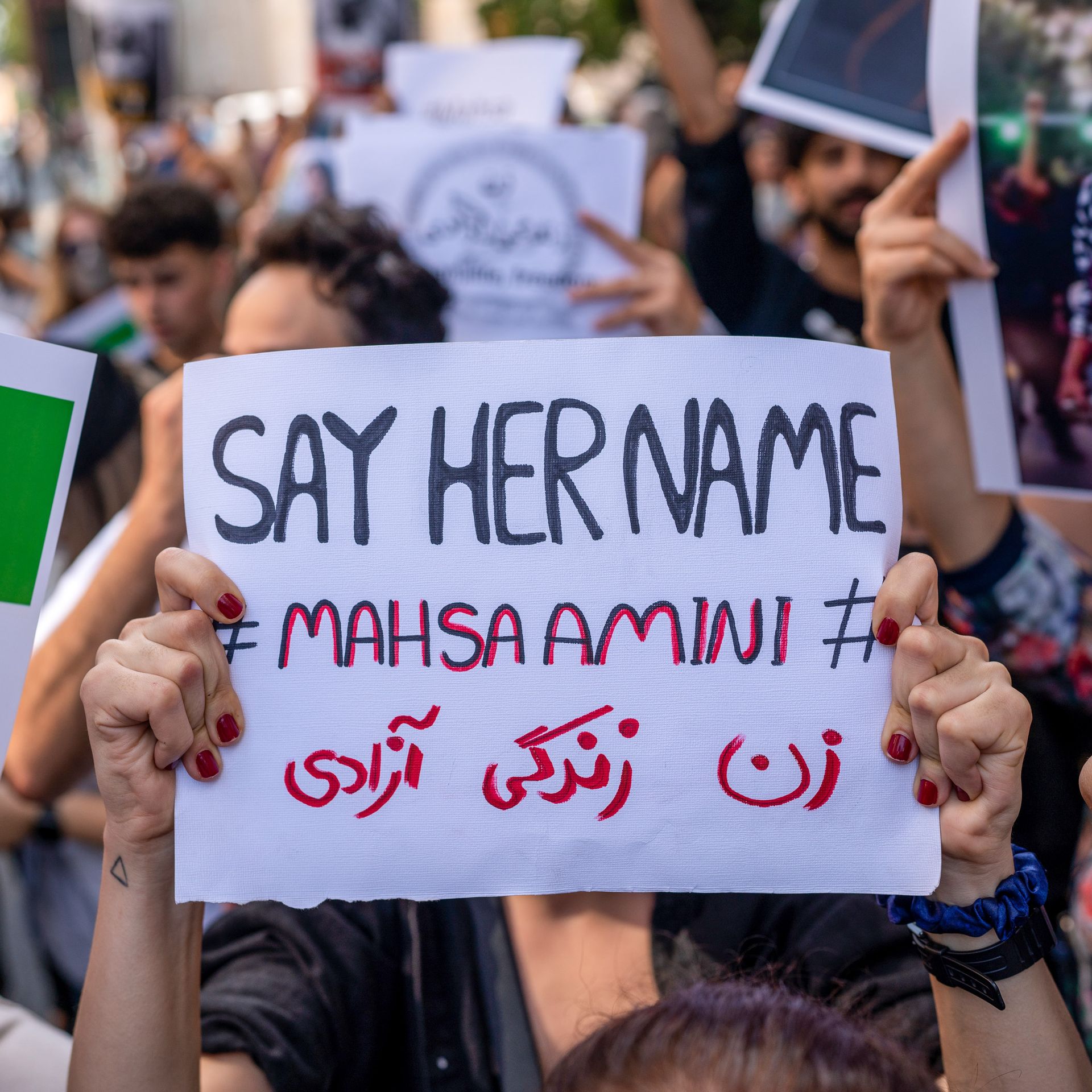 Protester holding a sign reading "Say her name: Mahsa Amini"