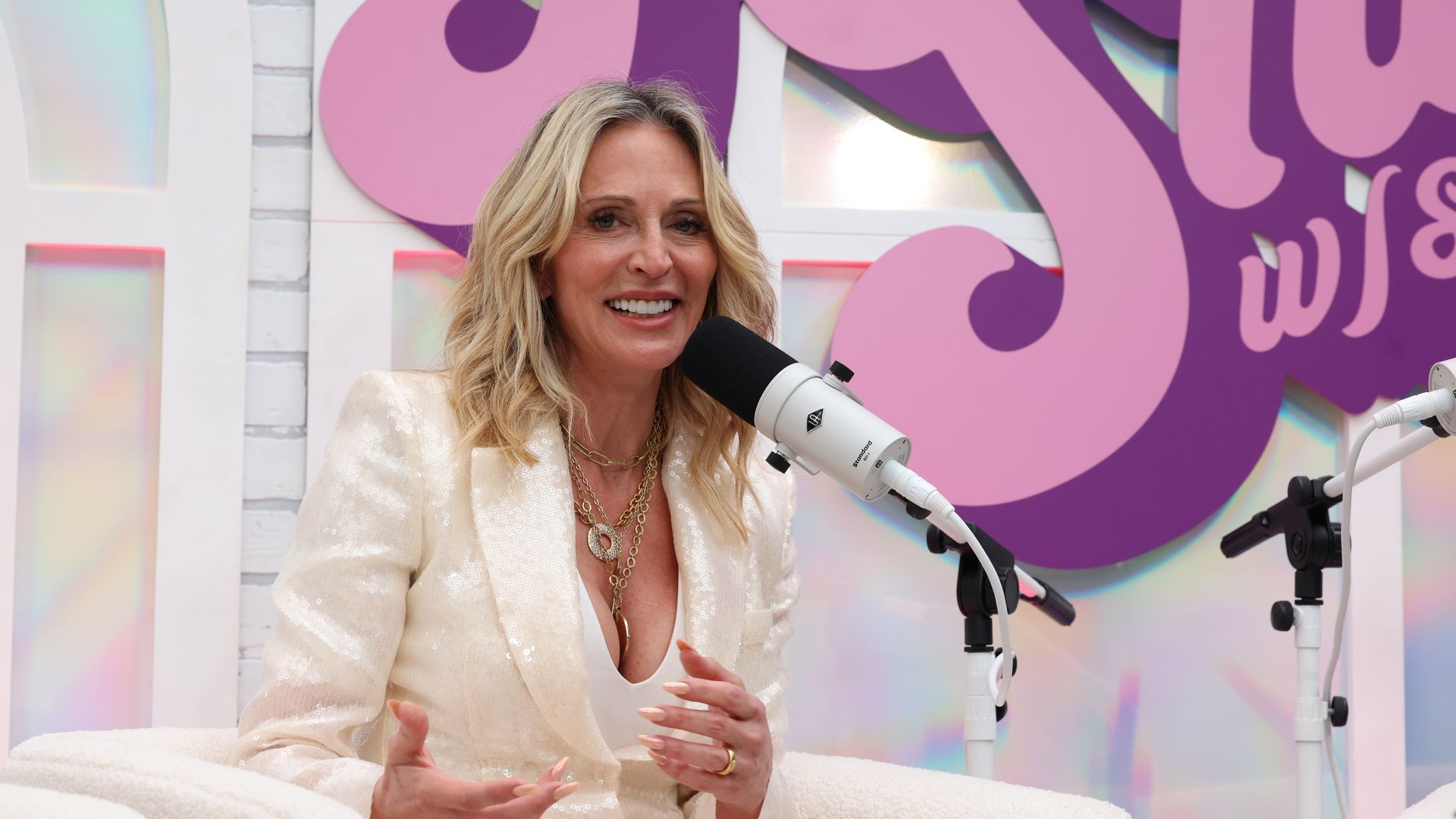 Suzy Batiz speaks into a microphone with the words "Holy shit" behind her.