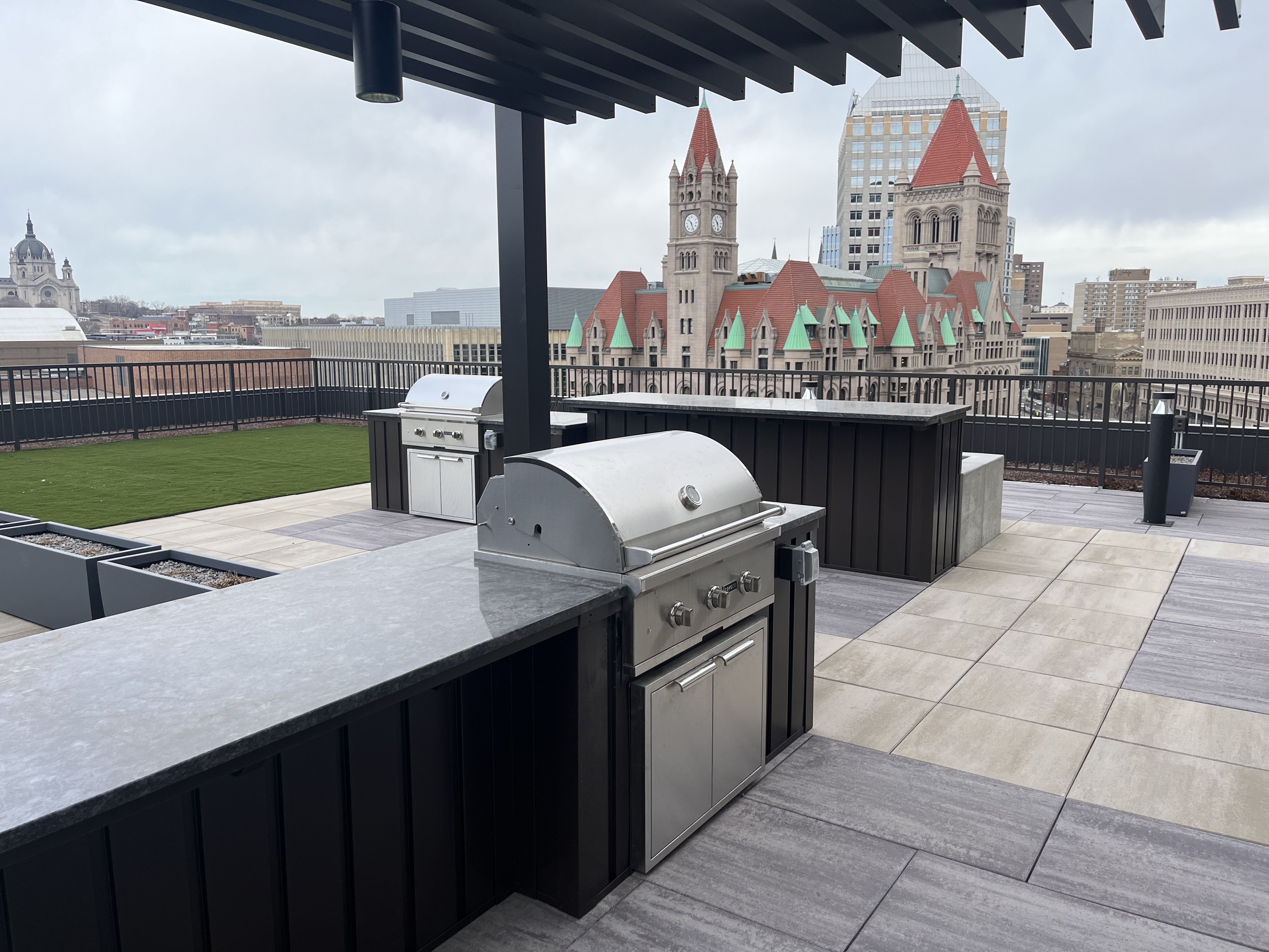 A photo showing a roof deck with grills and a green space.