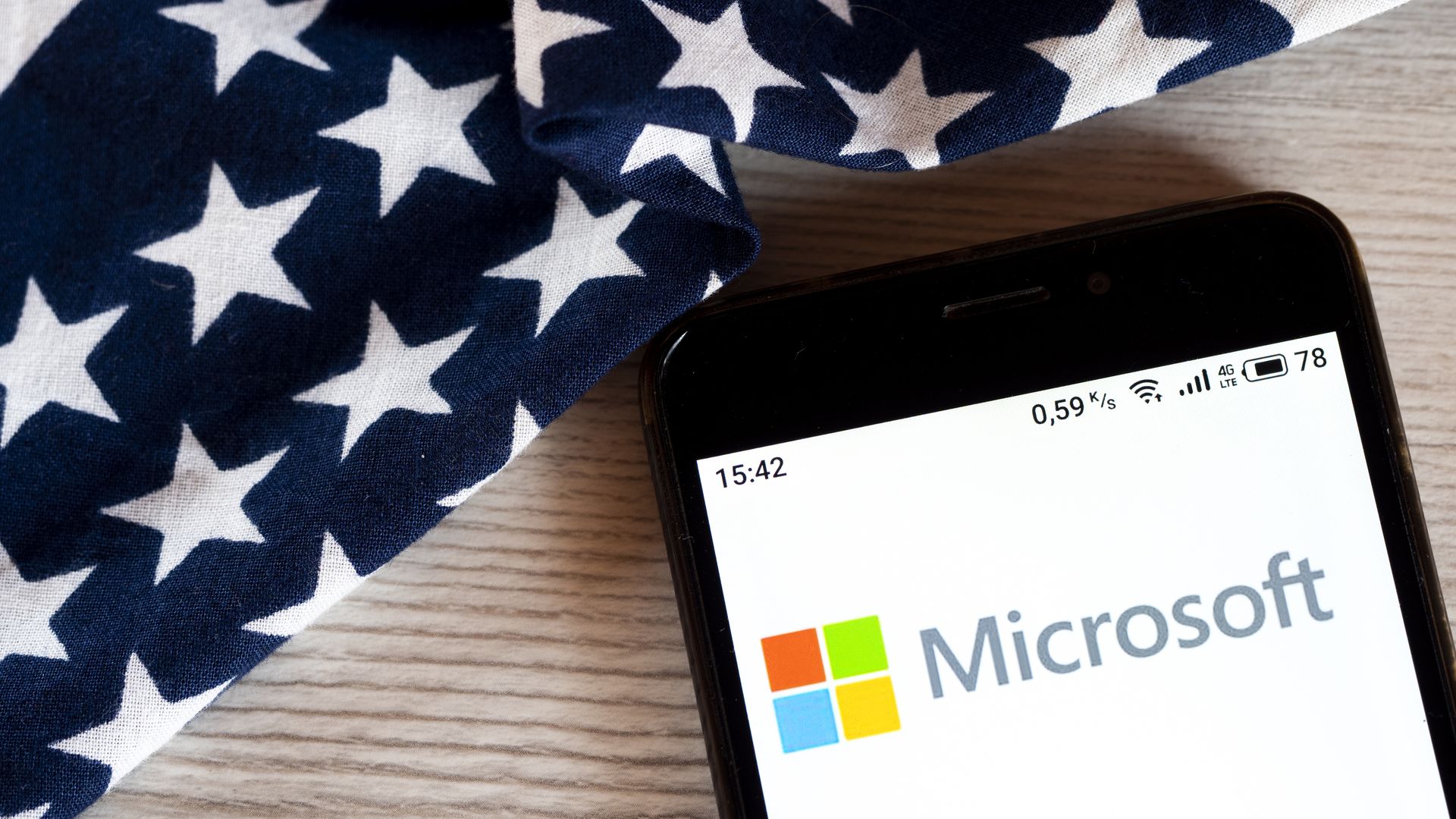 A photo of a smartphone displaying the Microsoft logo, with the American flag behind it