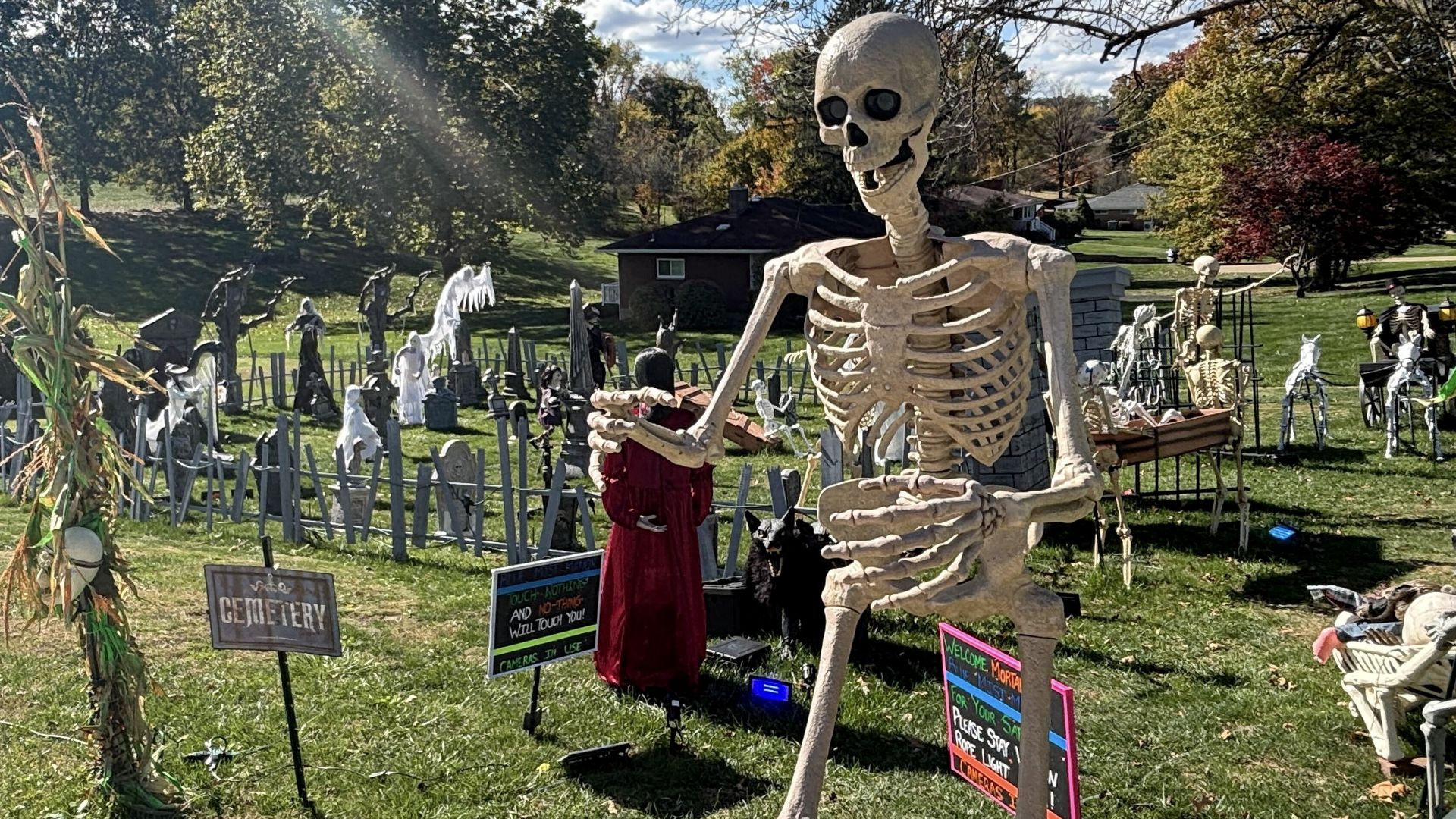 Outdoor Halloween display with large skeleton, ghost figures, tombstones, signs.