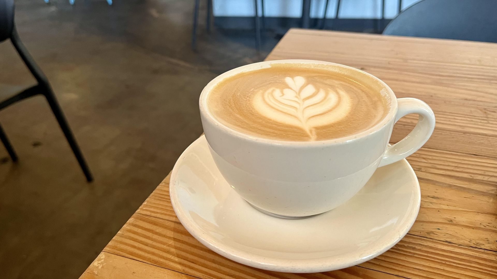 A latte sits on a saucer on a wooden table. 