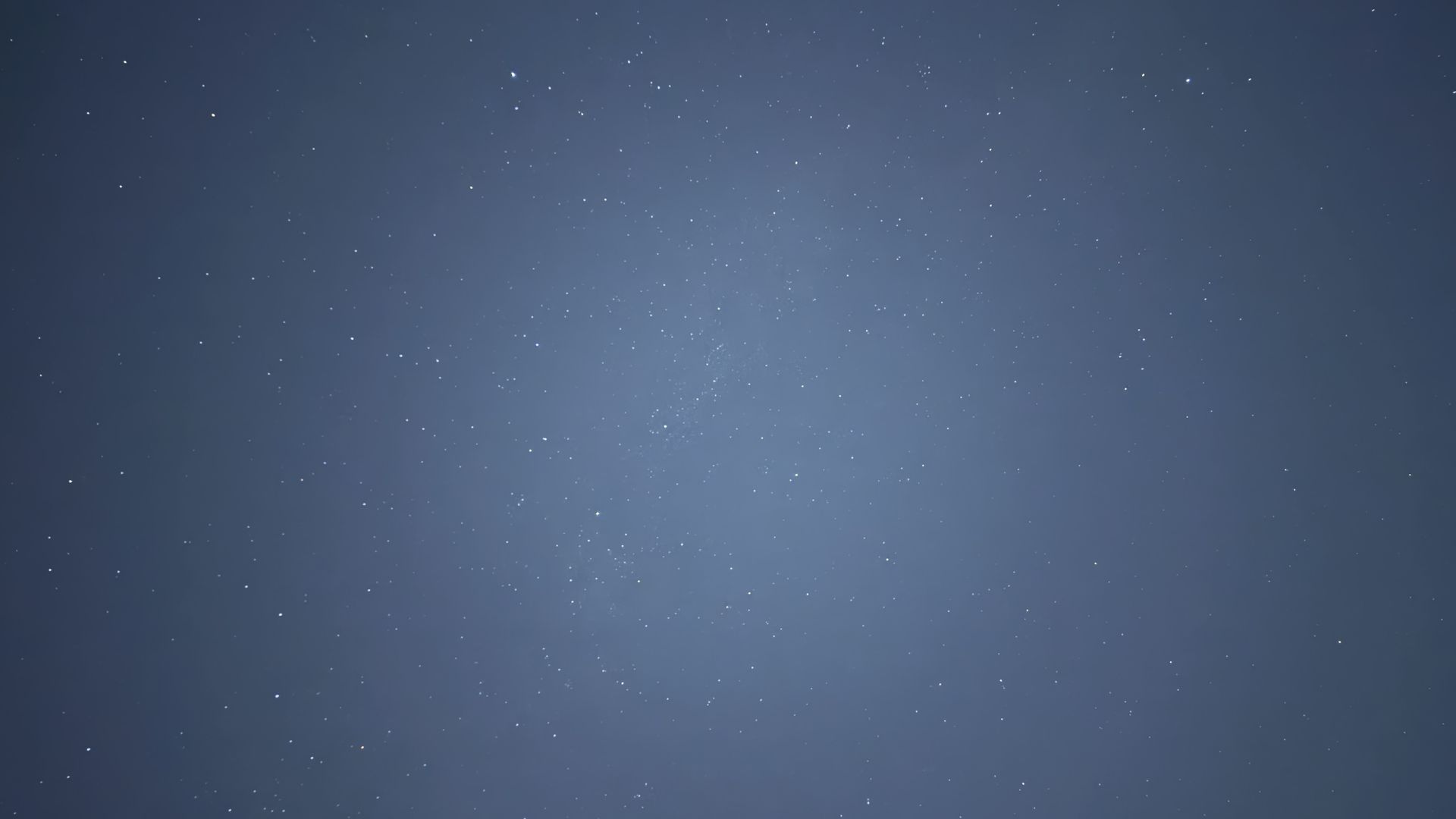Wide view of a dark blue night sky dotted with many white stars, a faint Milky Way glow near the center, creating a serene celestial panorama.