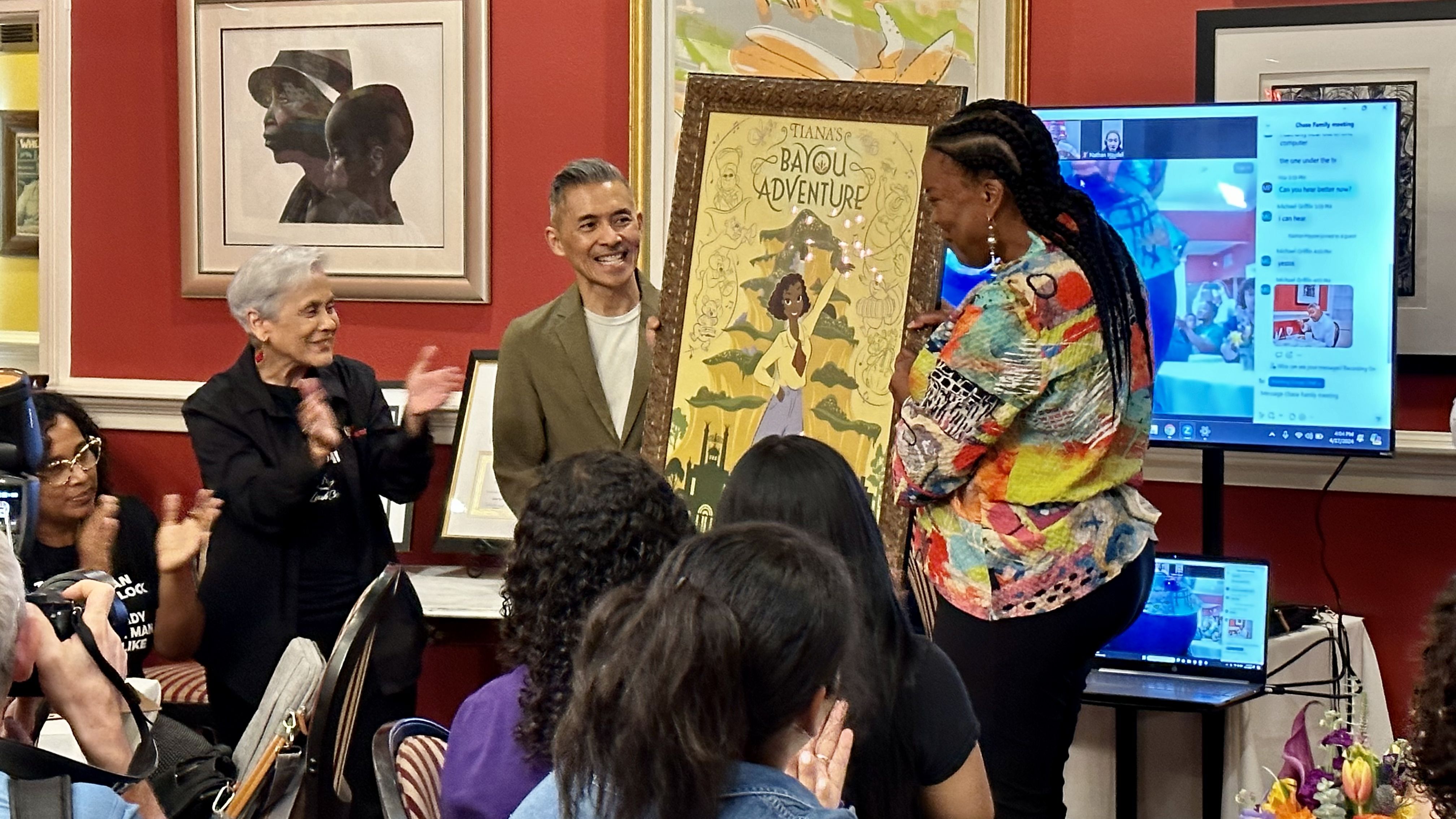 Disney imagineers present Stella Chase Reese with a poster from Tiana's Bayou Adventure.