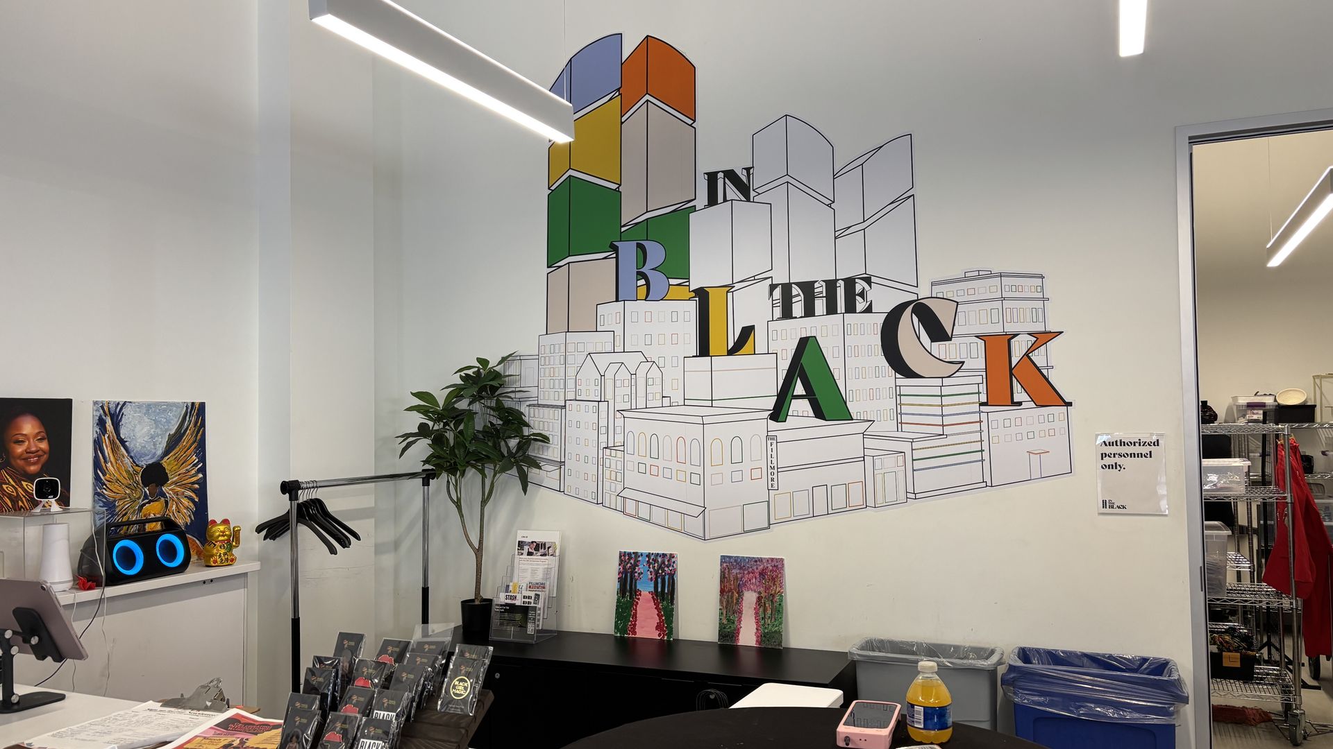 Bright office wall mural of stacked city blocks forming a skyline in blue, orange, yellow, and green; letters spell "BUILDING BLOCKS". A plant, coat rack, desk, and devices sit below.