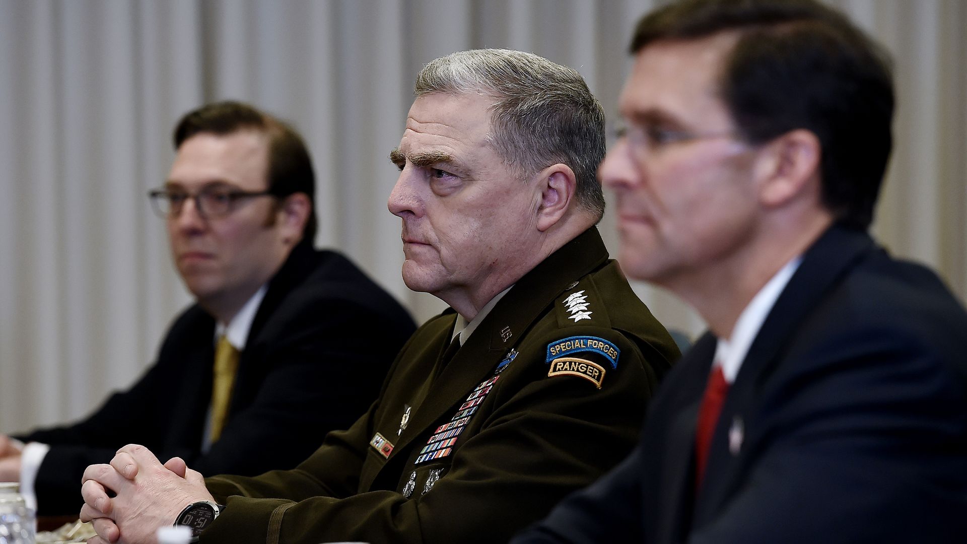 In this image, several men in formal military dress sit next to each other at a long table while facing the same direction 
