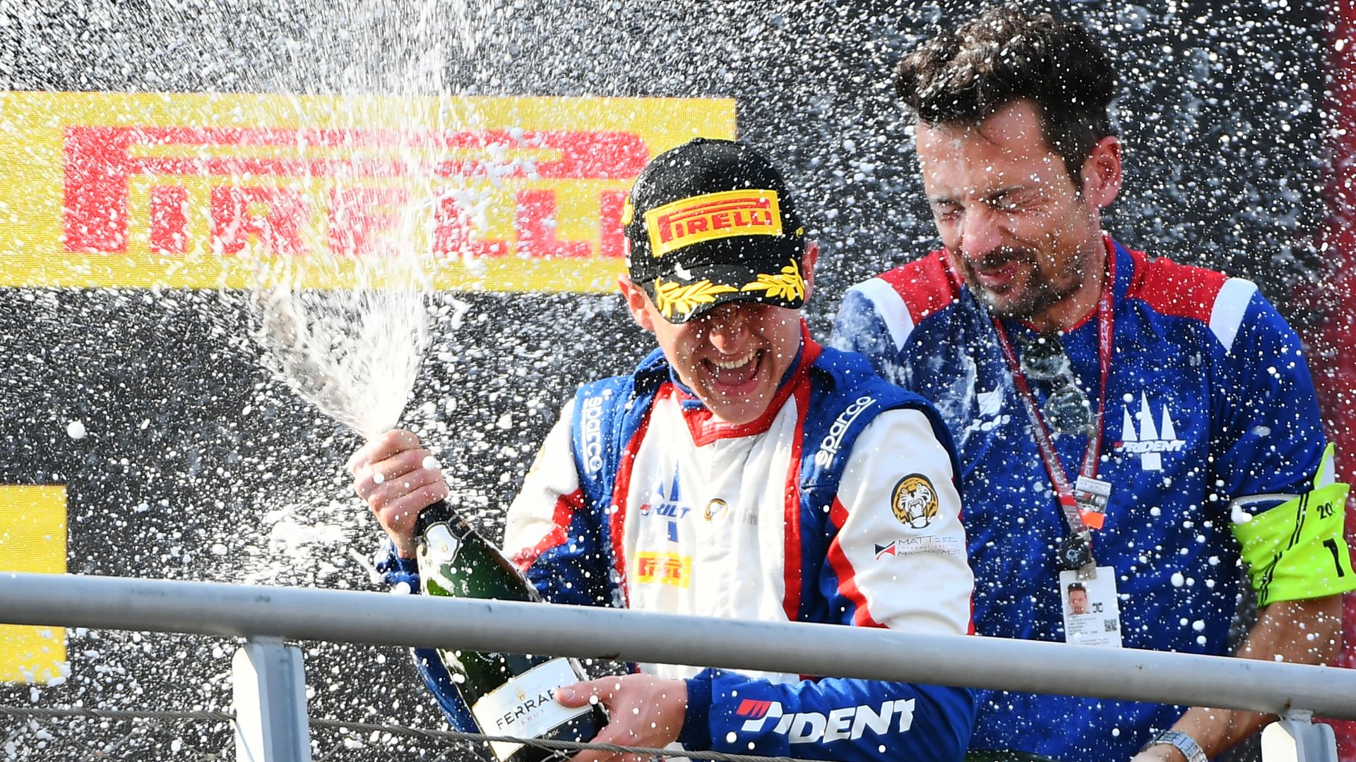 Race car drivers celebrate by popping a bottle of champagne.