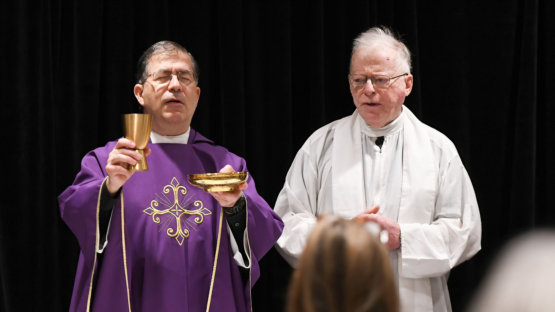 Priest with his eyes closed holding a cup and plate.