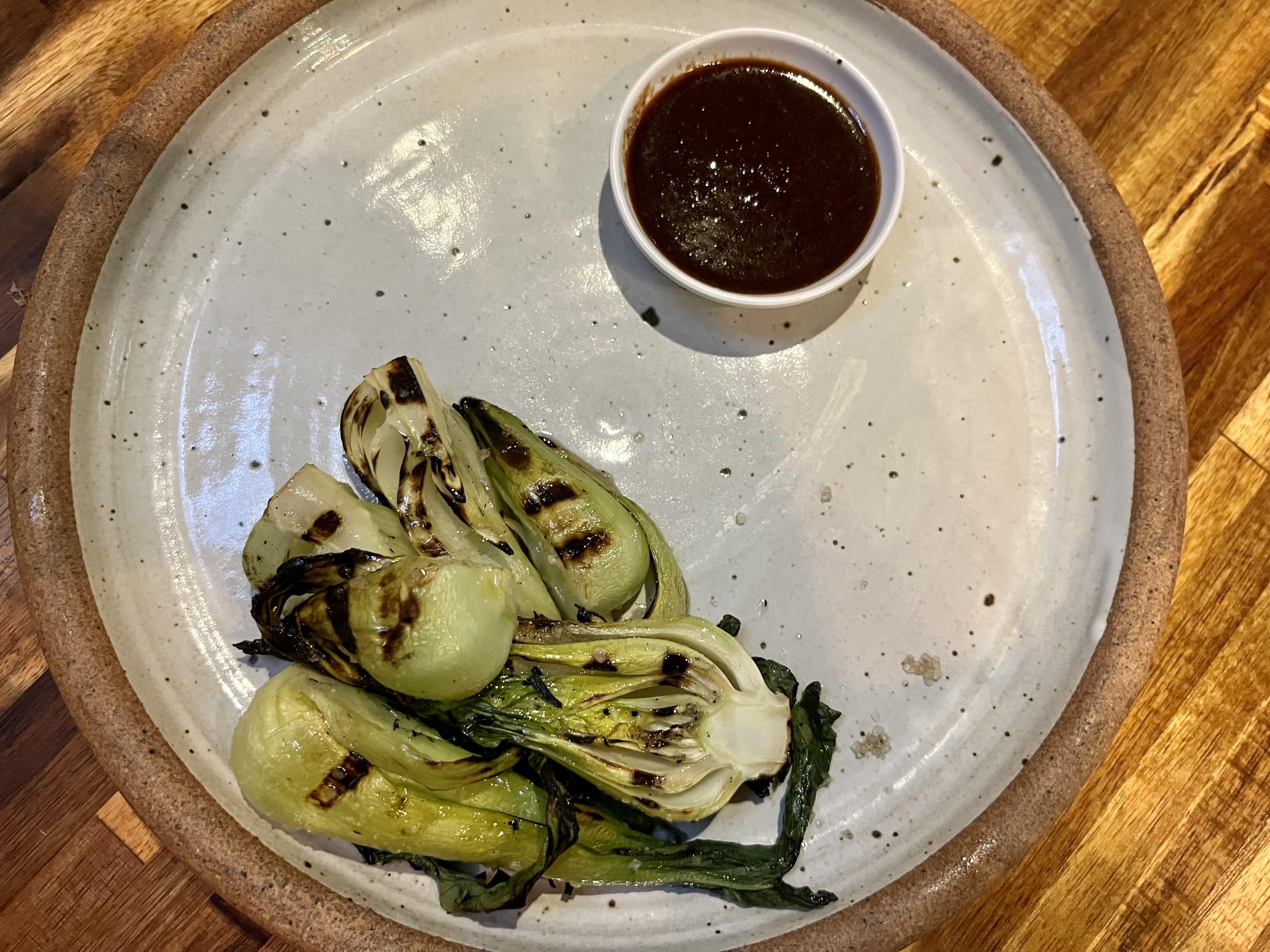 A gray stone plate featuring charred bok choy and a black garlic dipping sauce.