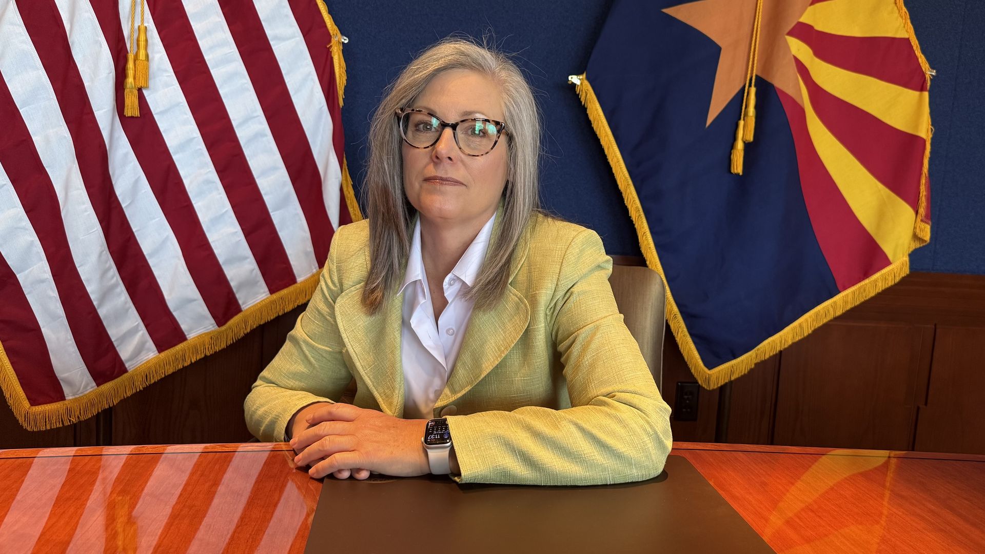 Katie Hobbs sits at a table with her arms crossed in front of her on the table. 