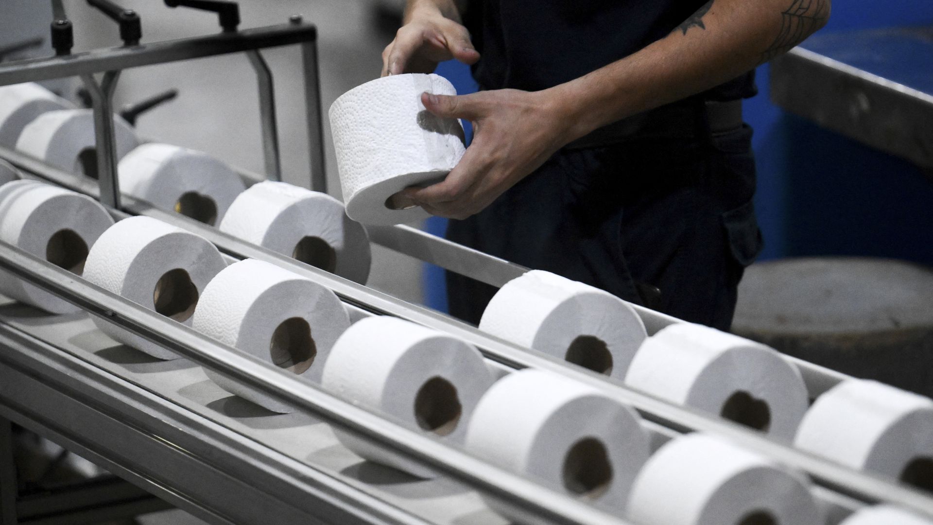 A person inspects a roll of toilet paper on an assembly line