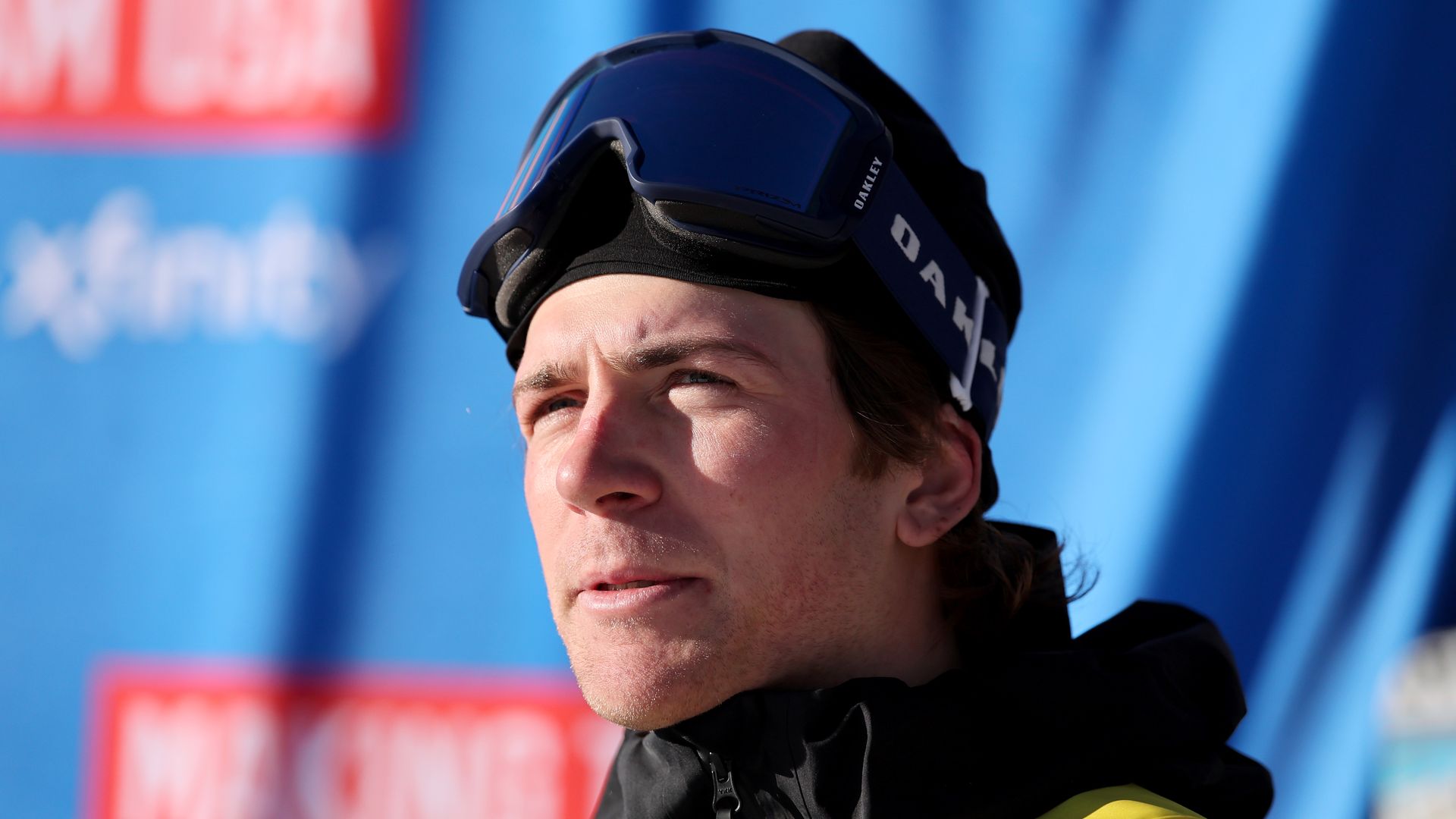 A headshot of a skier with a black hat and goggles standing in front of a blue screen