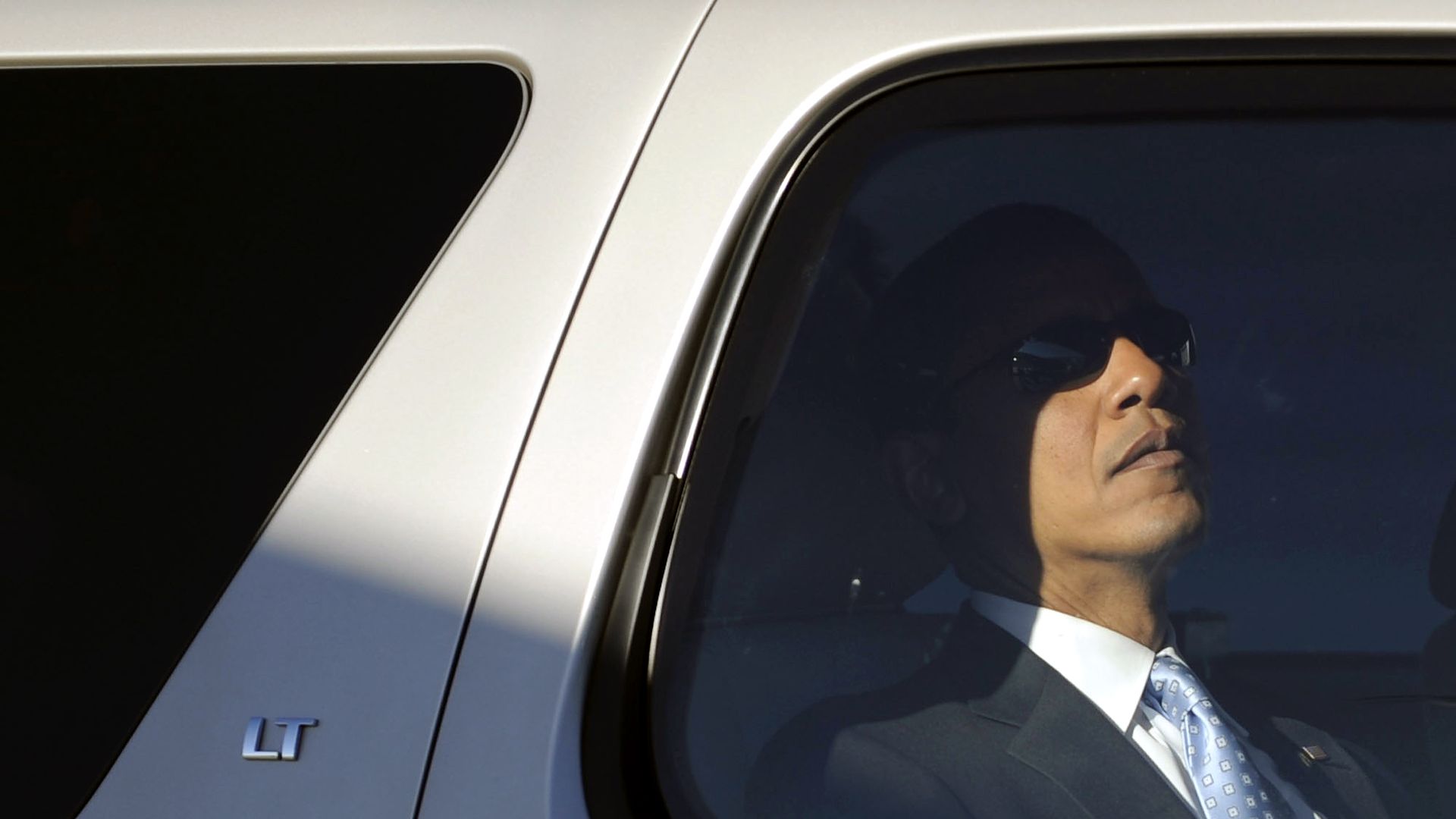 Obama wears sunglasses in the back seat of a car