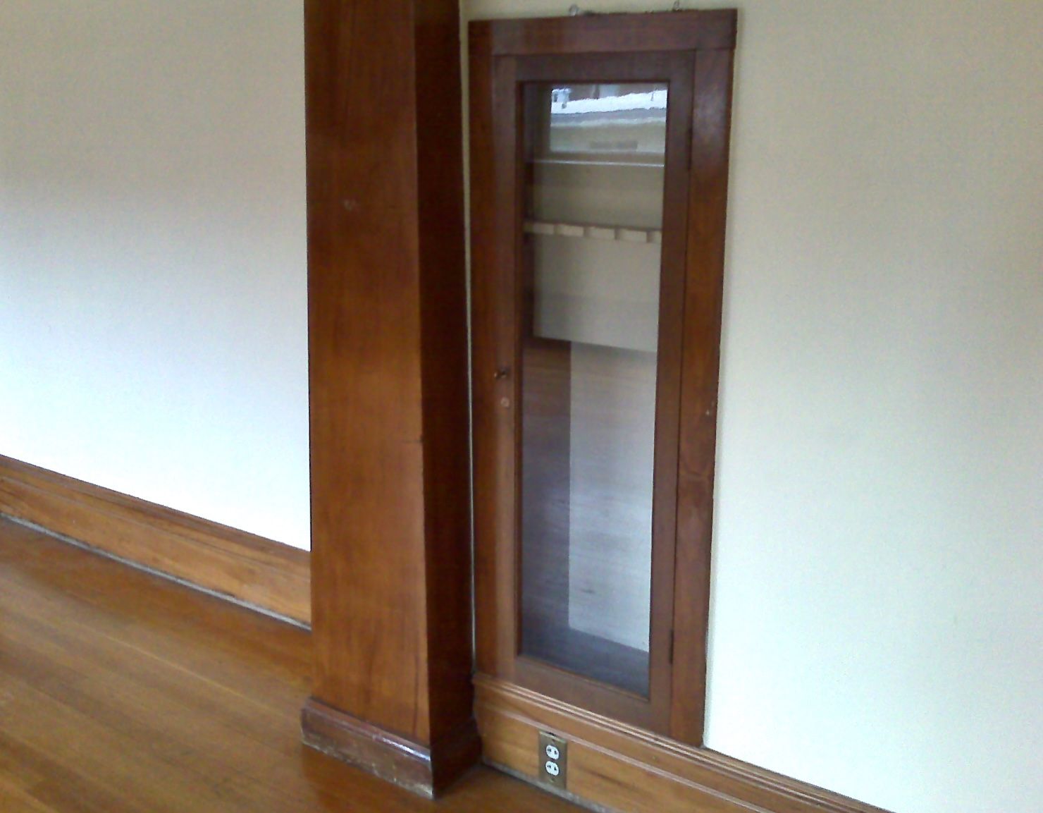 A gun cabinet with a glass door, built into a wall. 