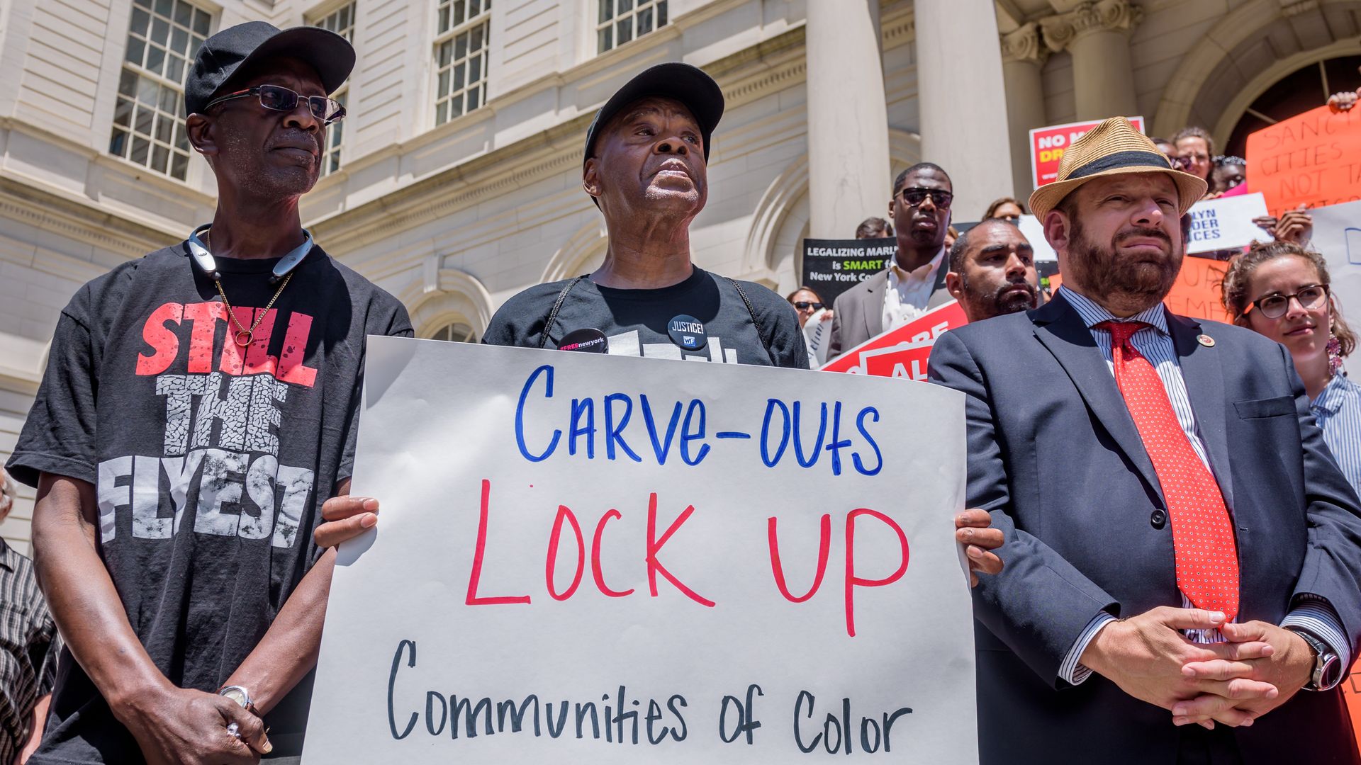 Advocates hold up a sign that says "Carve-outs lock up communities of color" to protest NYC marijuana policies