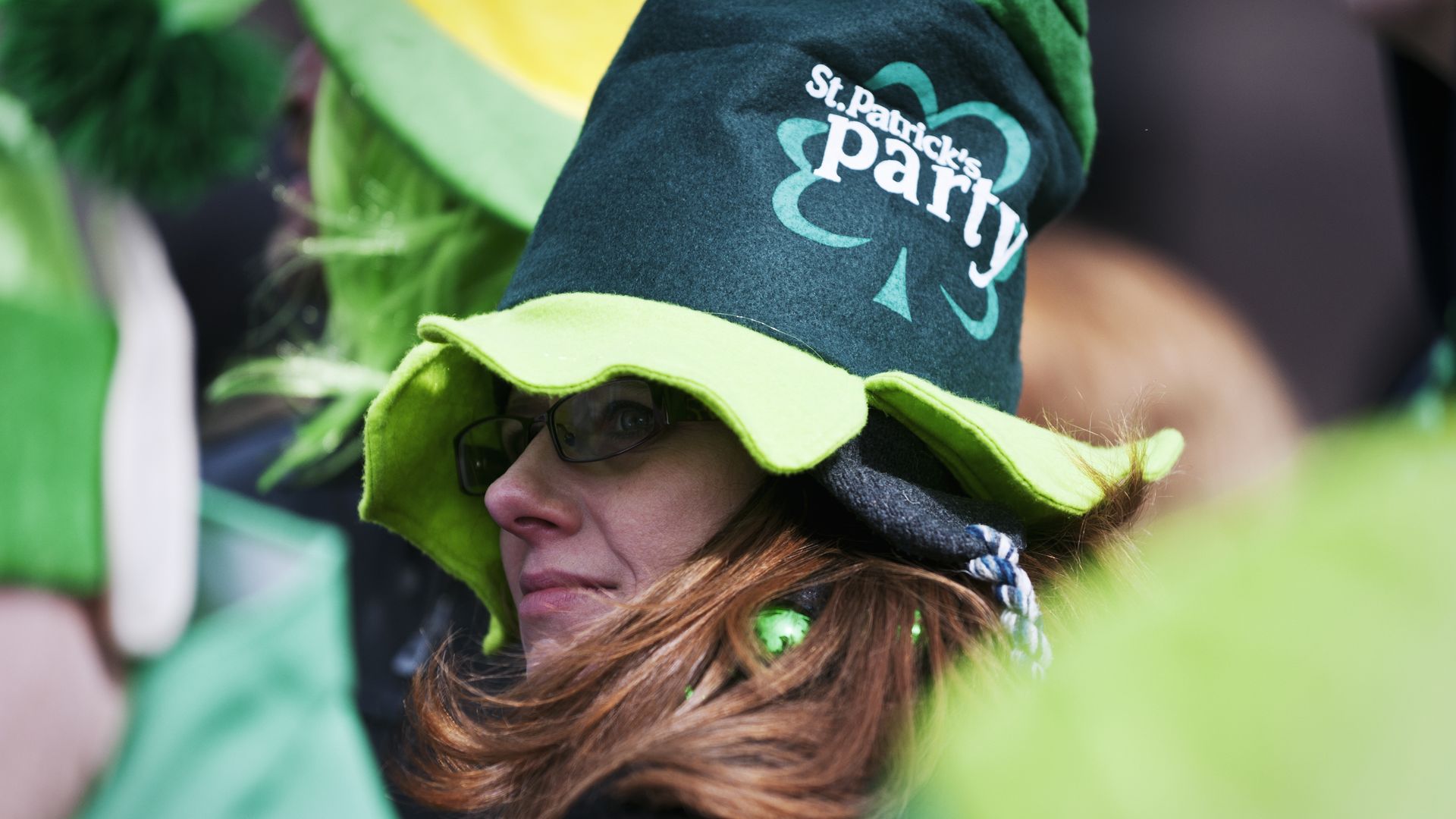 Woman wears a red St. Patrick's Day party hat in the middle of a parade crowd. 
