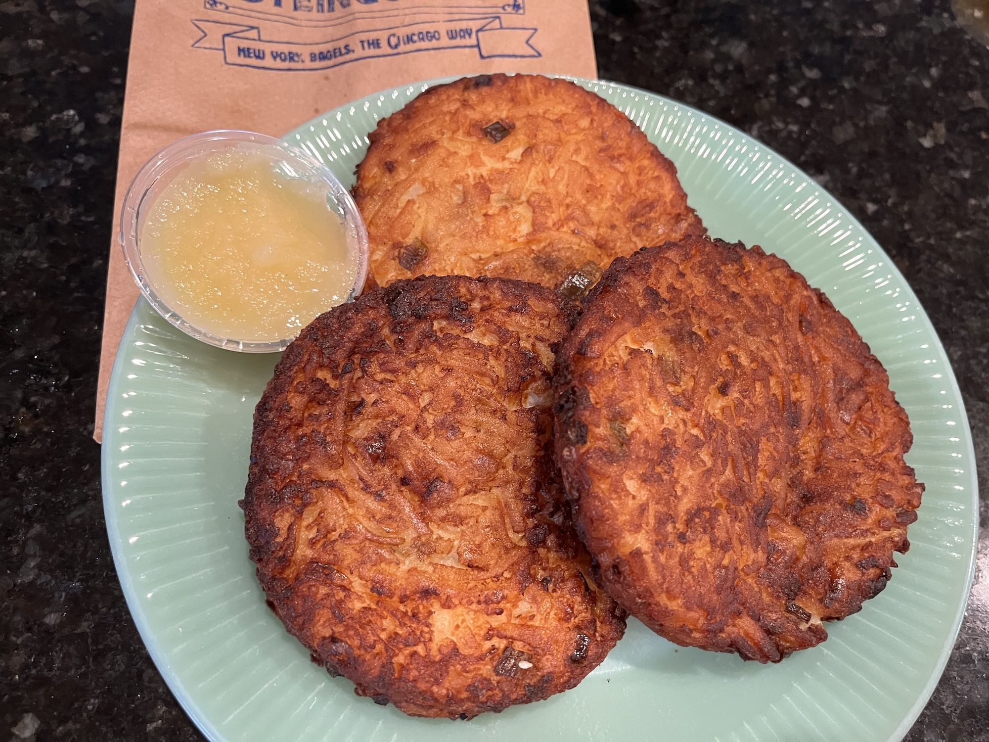 Three round potato pancakes on green plate with cup of applesauce.