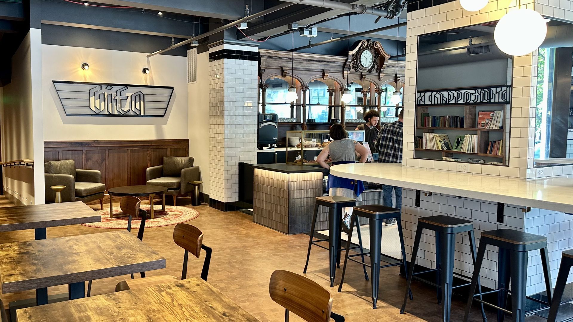 A sign says "Vita" above a seating area in a warm-toned space with woodwork and black and white subway tile.