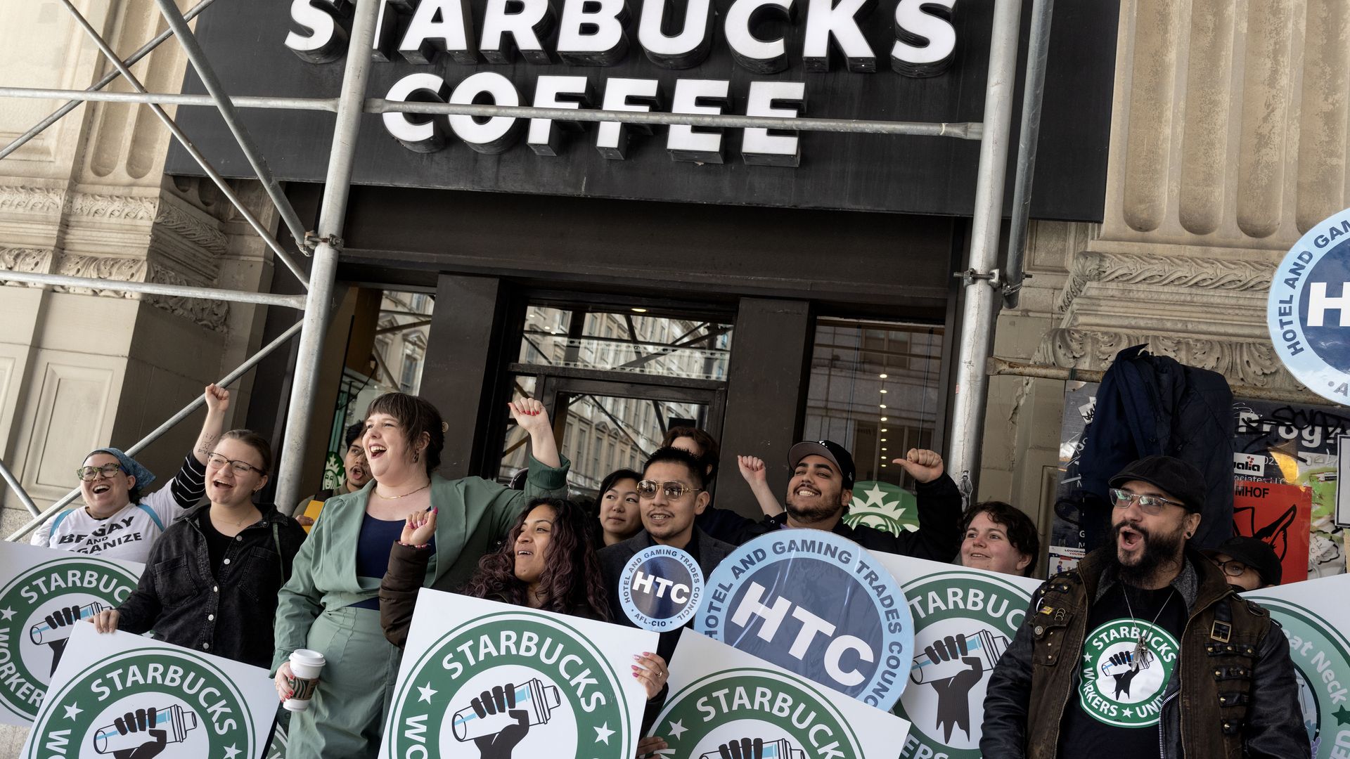 Starbucks union members and their supporters, including baristas who have just walked off the job, hold signs and picket in front of a Starbucks store.