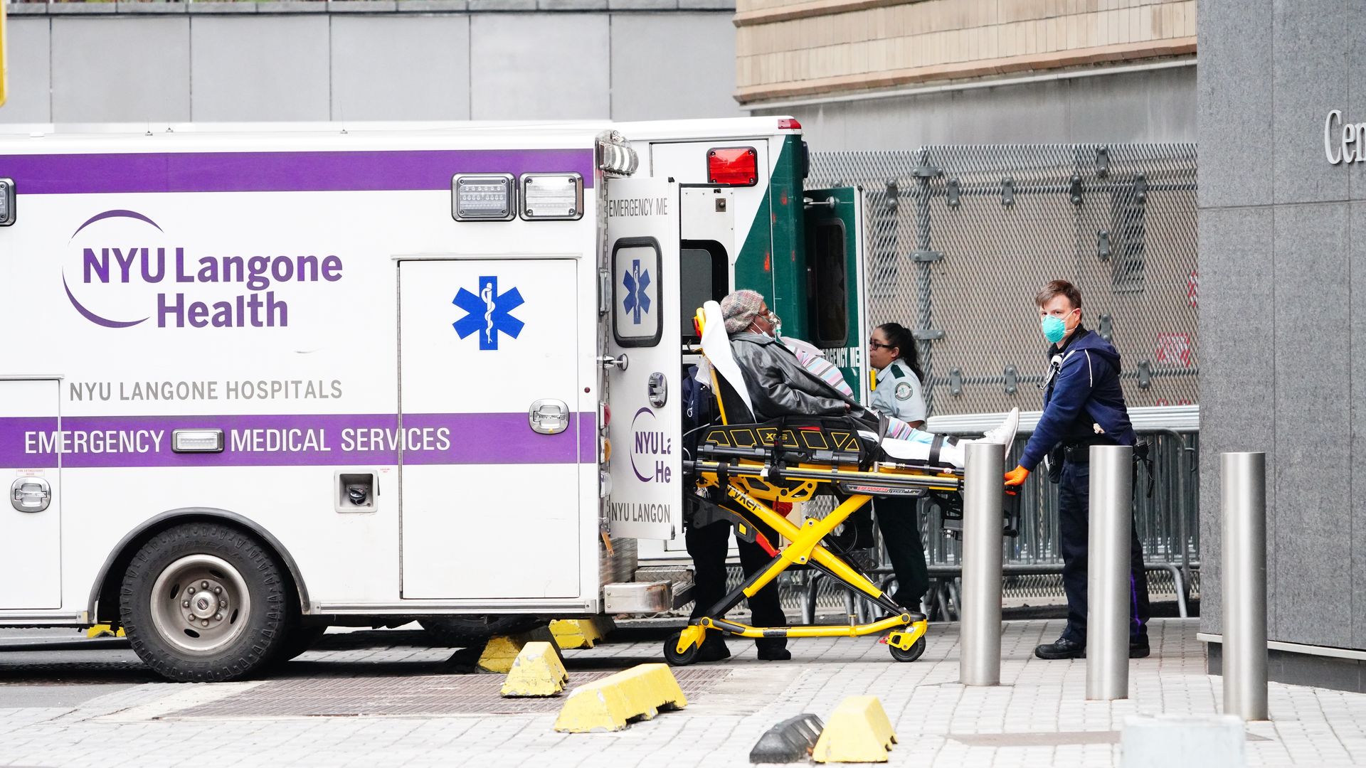 An elderly patient wearing a mask is seen being wheeled out of an ambulance