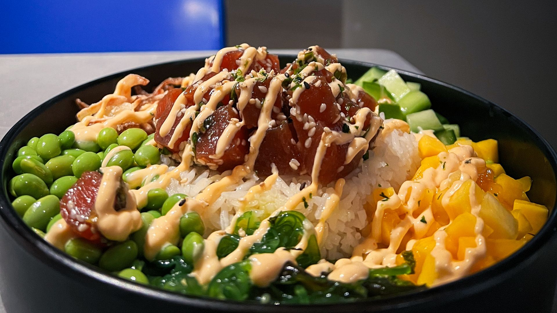 A bowl filled with rice, seaweed salad, mangoes, edamame, cucumbers and tuna. 