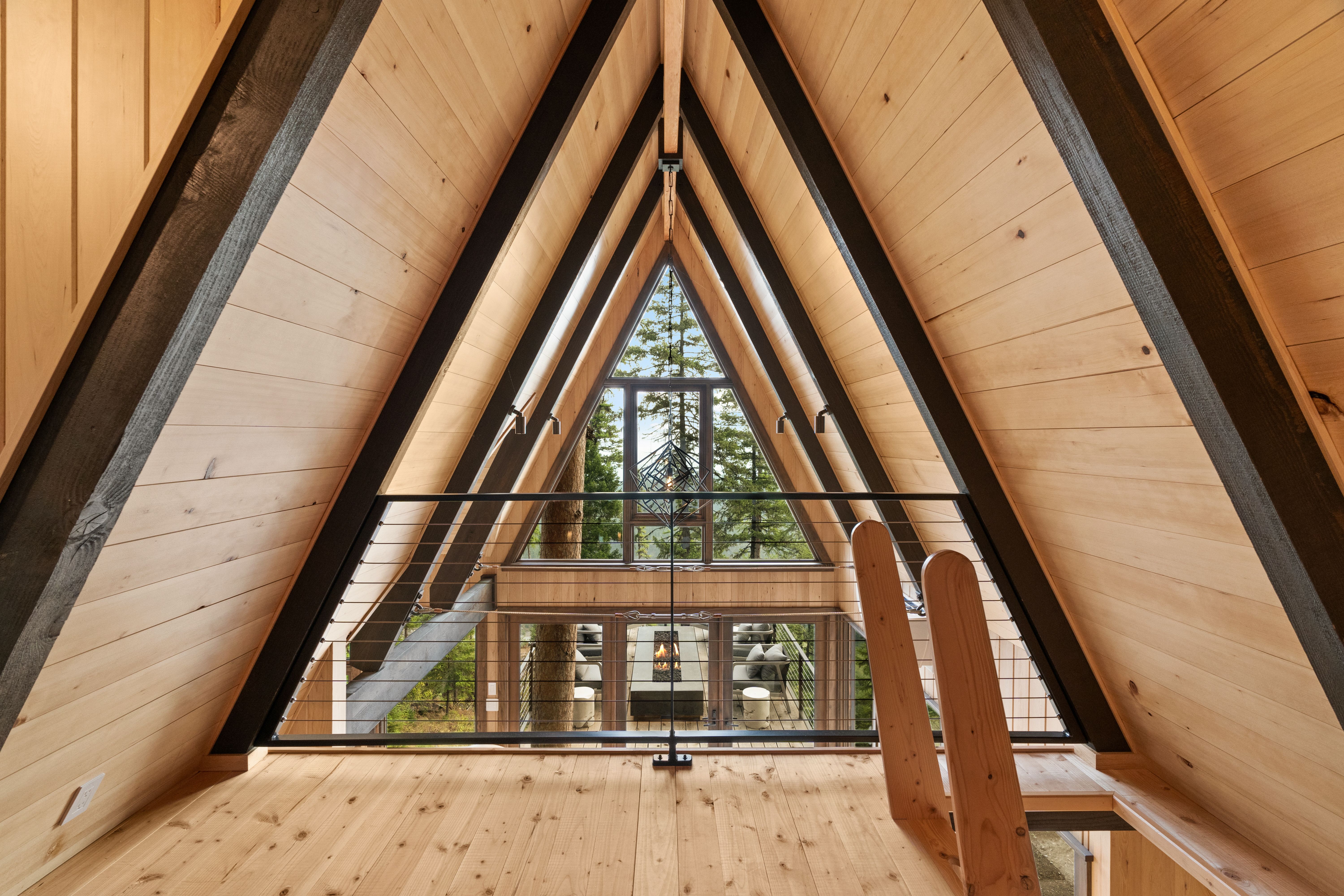 Triangle-shaped windows to the exterior are seen through the A-frame roof line from inside a house.