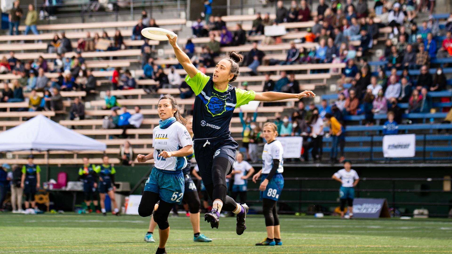 Female ultimate frisbee player soars in the air while making a catch.