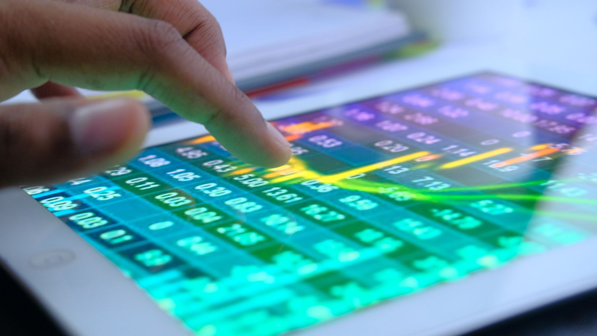 In this image, a hand controls the touch screen on an iPad showing stock and investment numbers.
