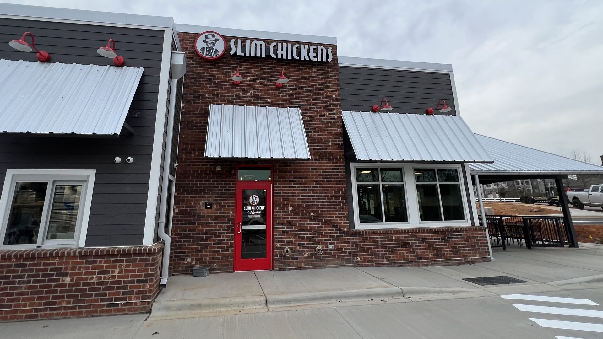 Brick building with covered outdoor patio. Signage on the roof reads "Slim Chickens"