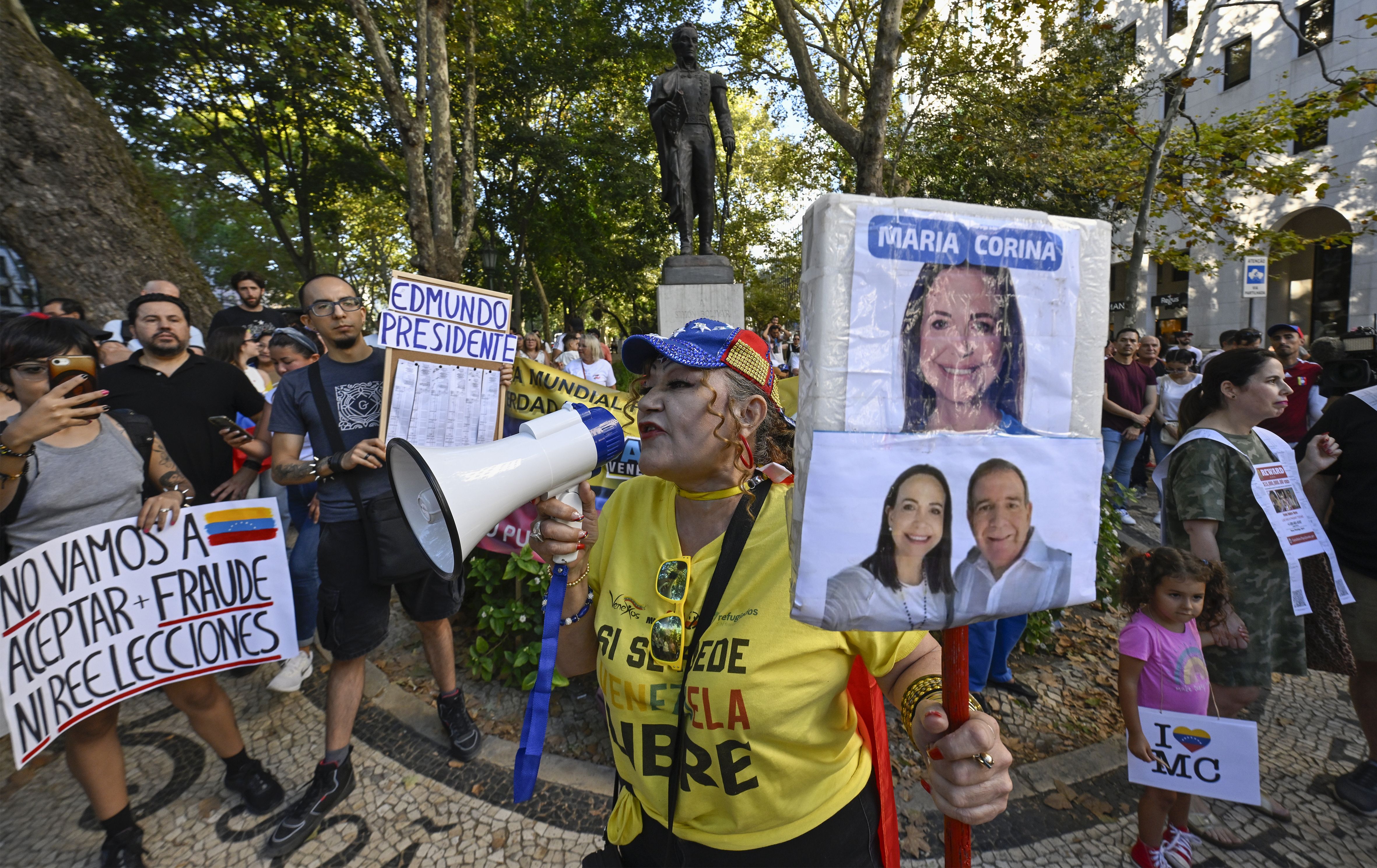 A woman in a yellow shirt holding a photo of the opposition leaders and holding a bullhorn protests in Portugal against Maduro 