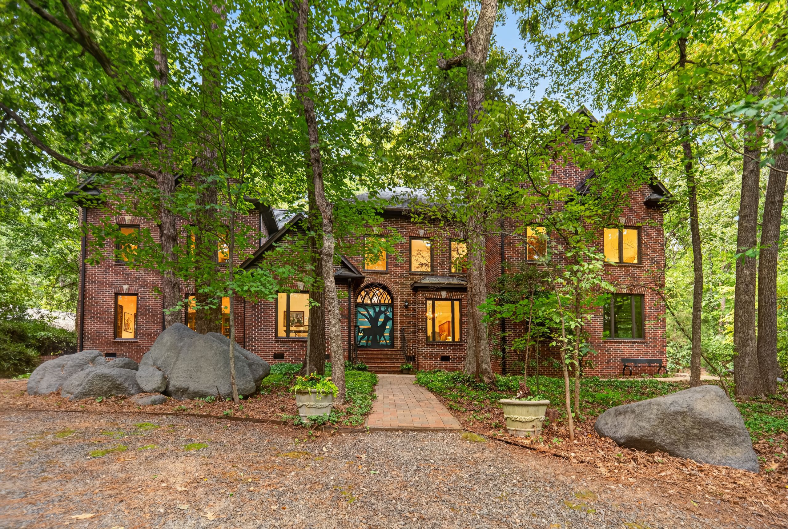 Large red-brick home surrounded by mature trees, with a brick walkway leading to the front entrance.