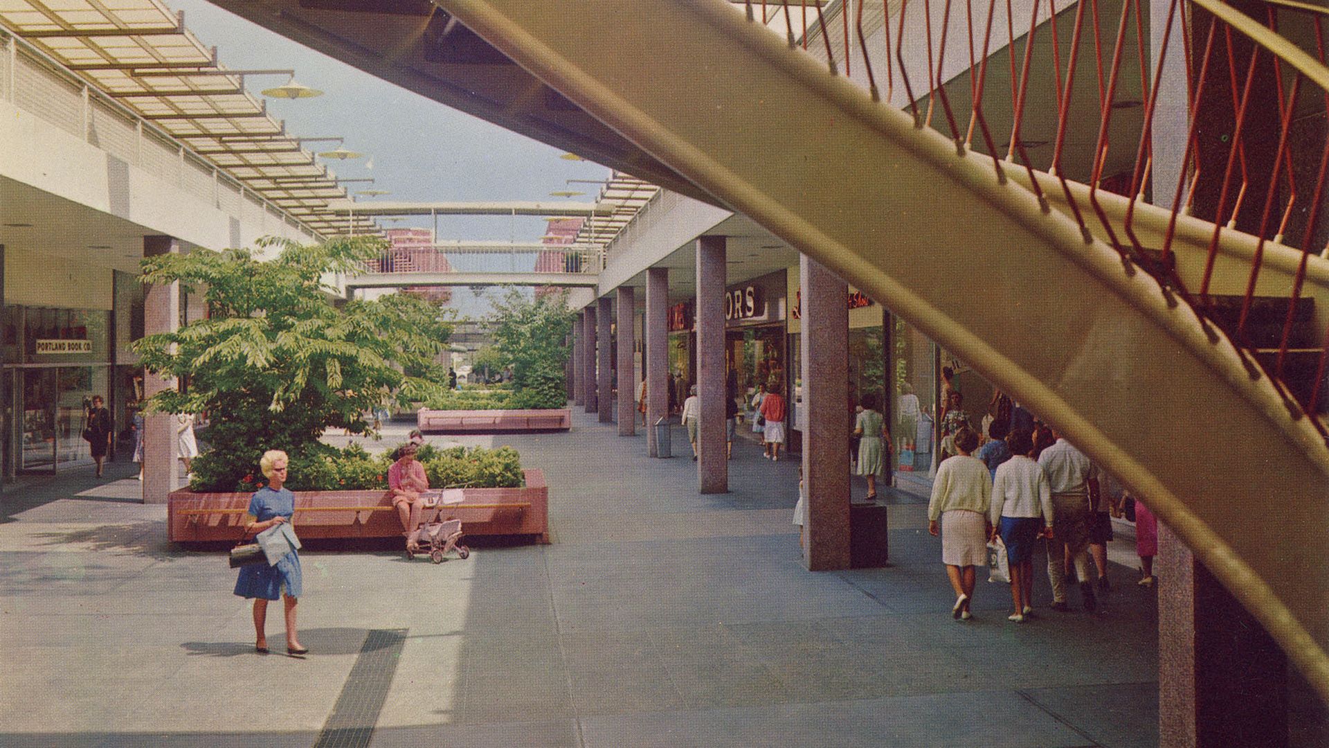 Outdoor shopping mall scene with people walking, a woman in blue holding a bag, a woman sitting on a bench with a stroller, and a yellow curved escalator railing in foreground.