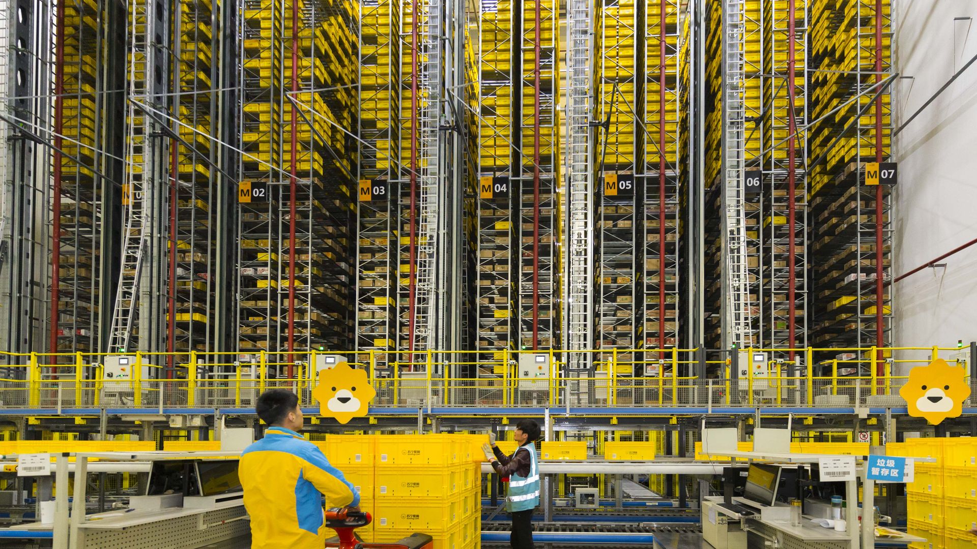 Two workers stand in a warehouse that is piled high with parcels